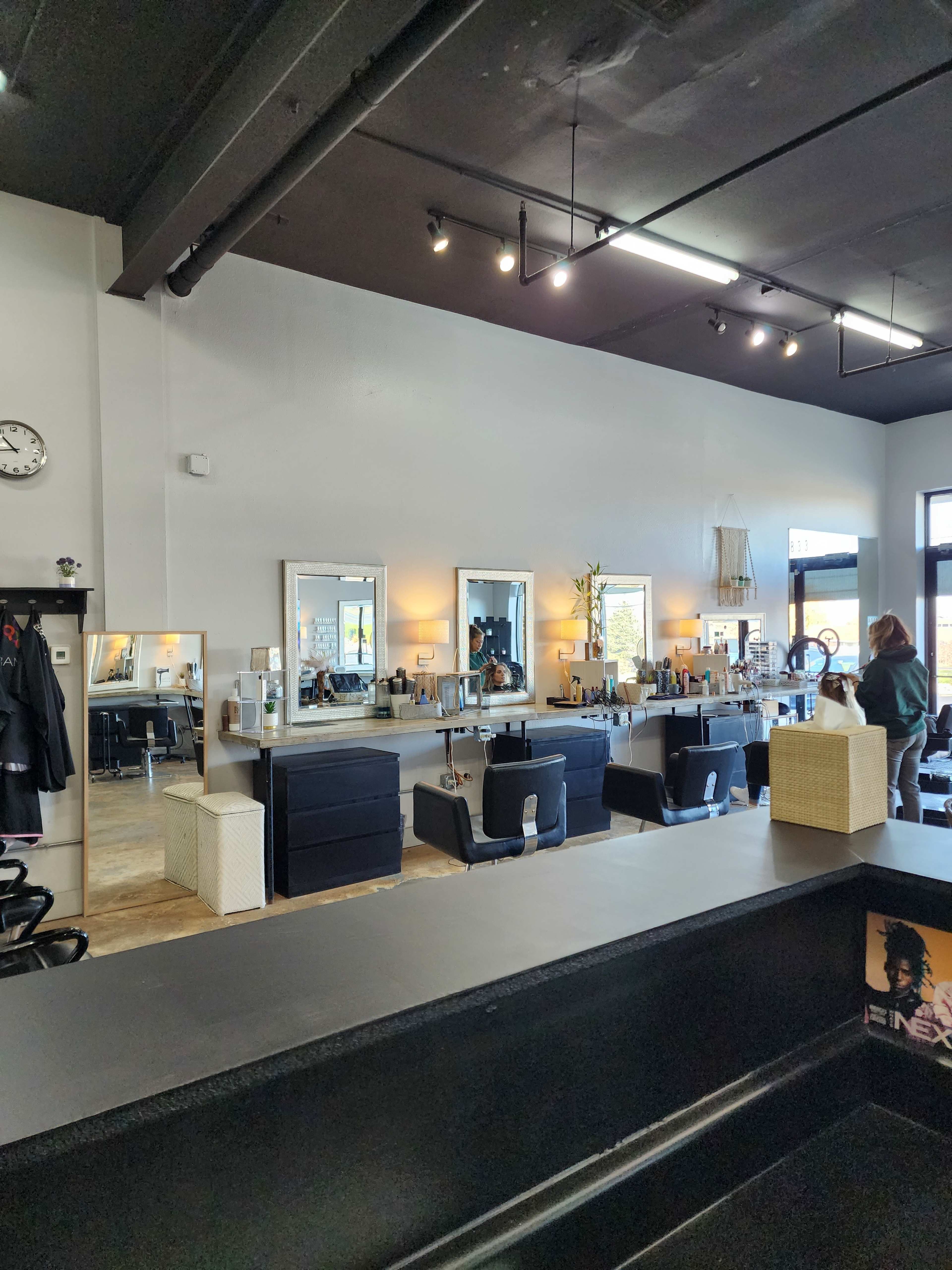 A modern hair salon interior with black styling chairs, large mirrors, and a reception area with a sleek counter.