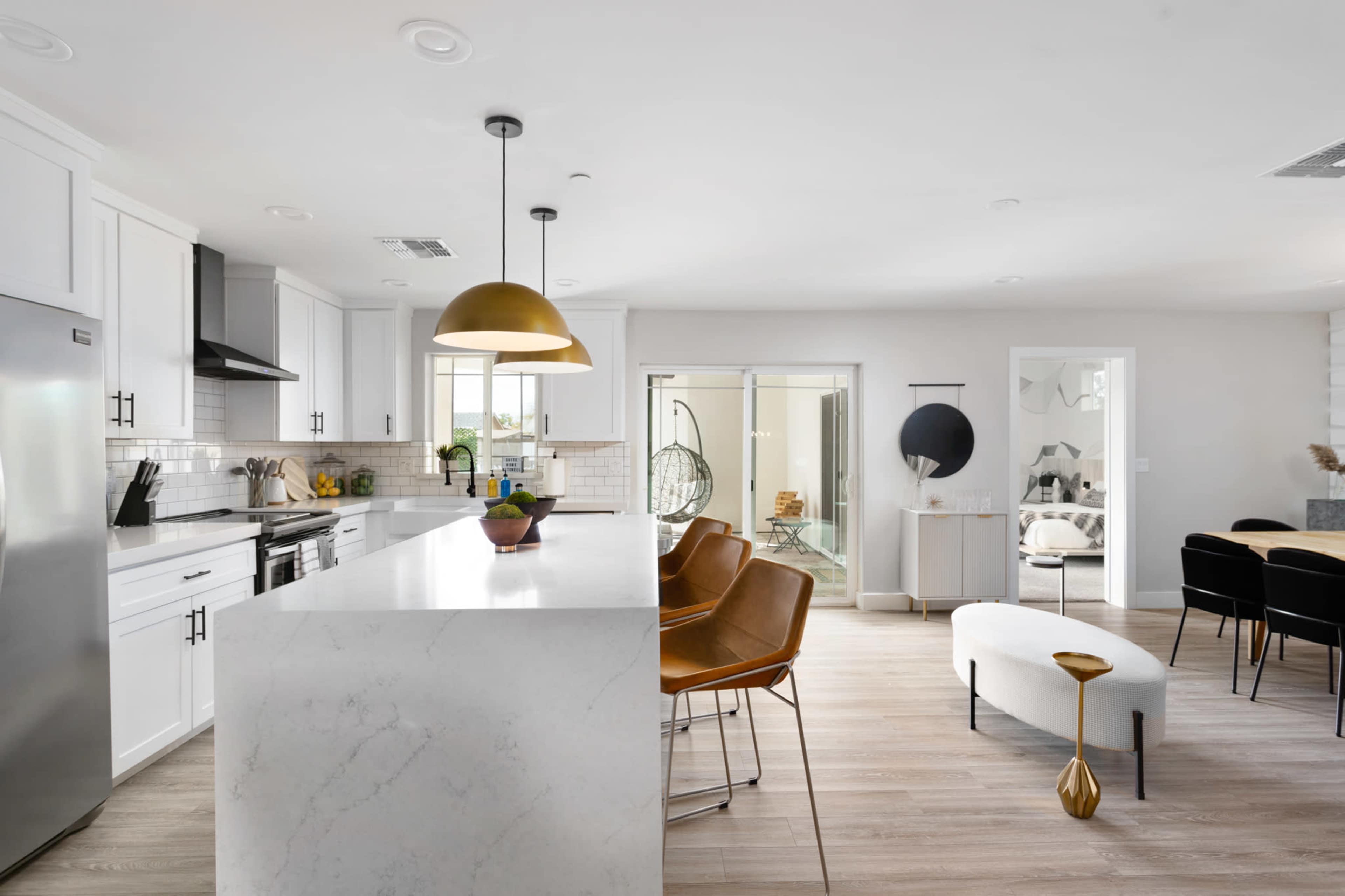 A modern kitchen features white cabinetry, a large marble island with bar stools, and an open layout connecting to a dining area.