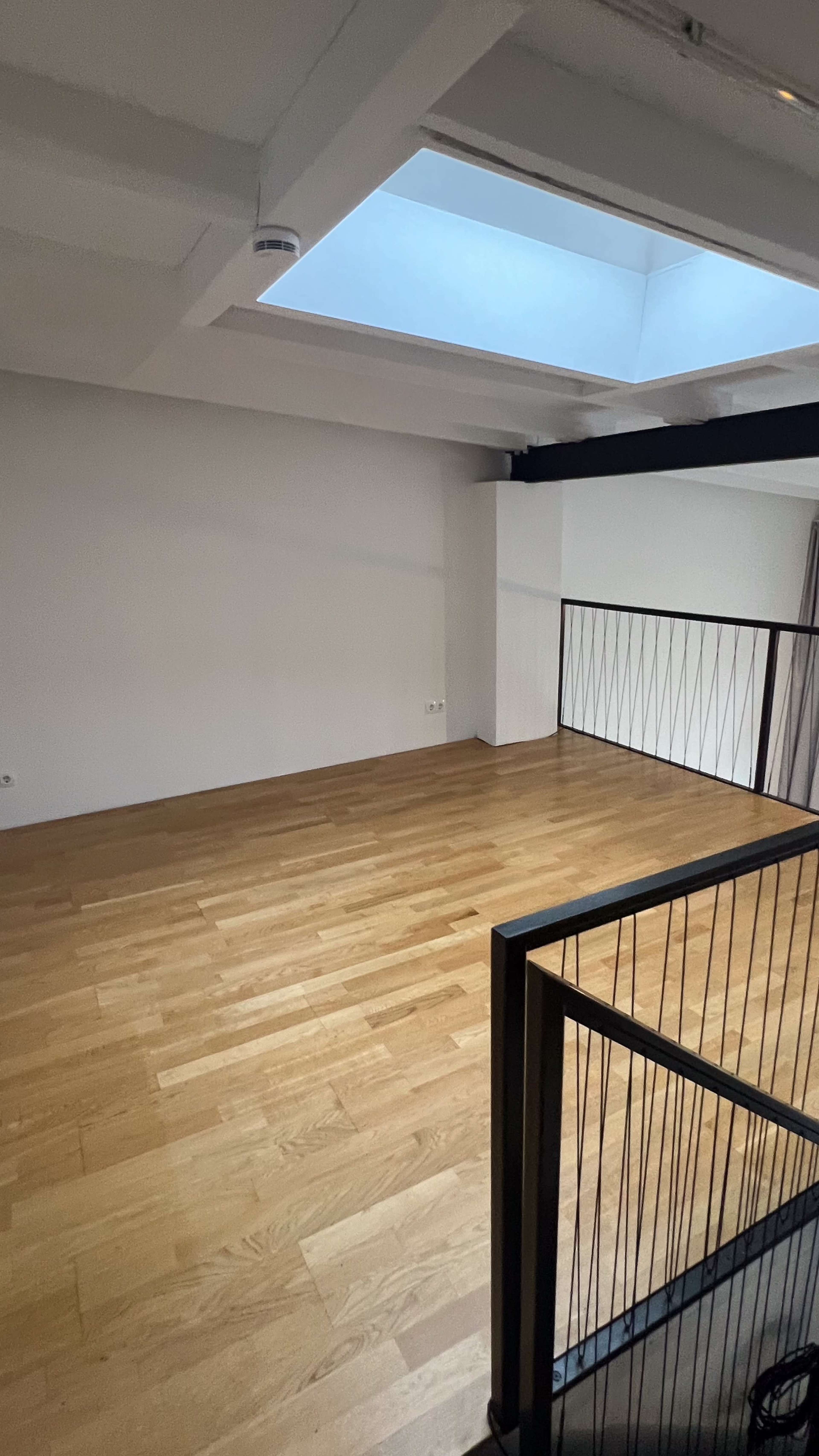 The image shows an empty room with polished wooden flooring, white walls, and a skylight above.