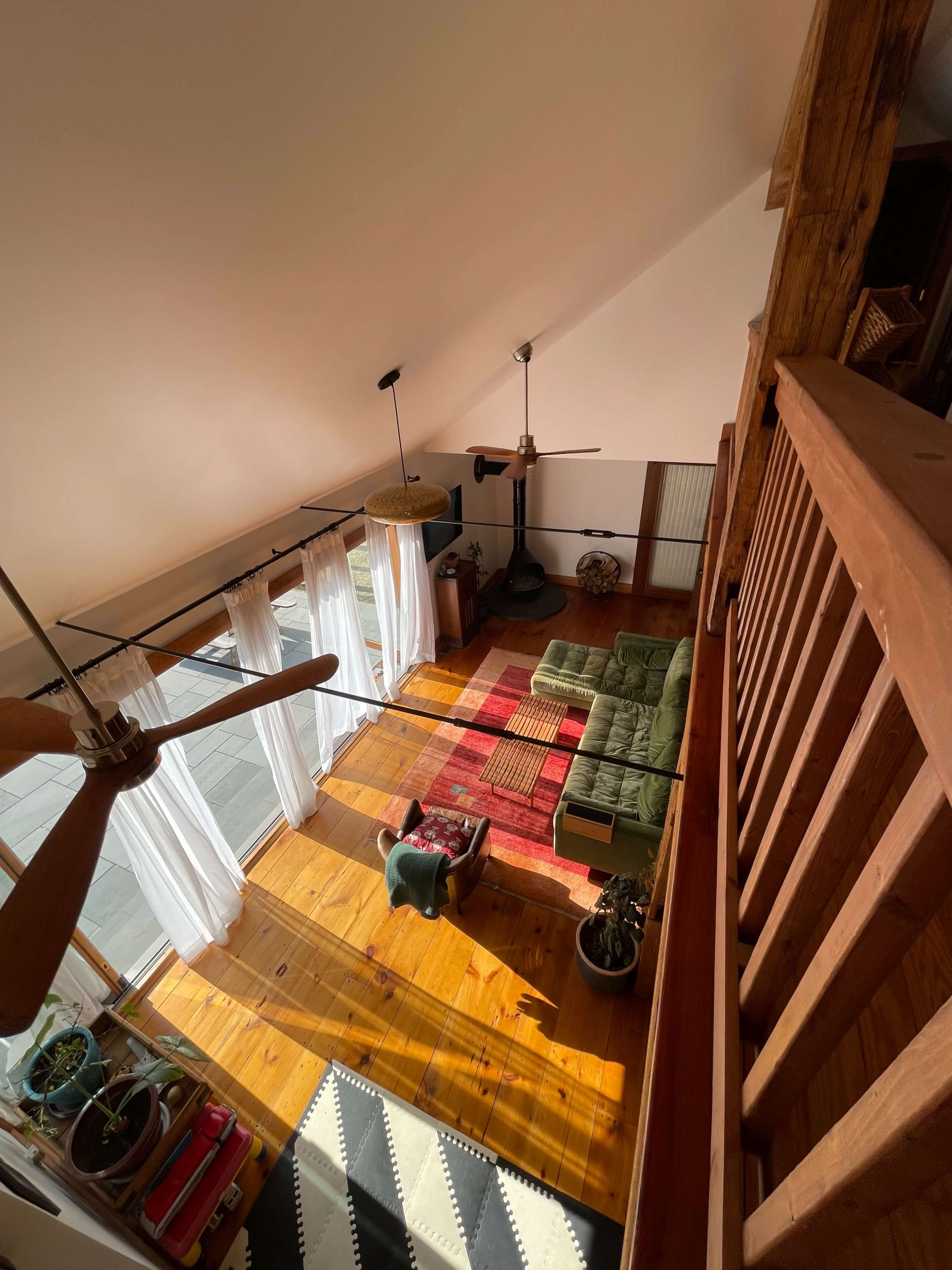 A spacious, well-lit living area with a green sectional sofa, a coffee table, and large windows that allow sunlight to illuminate the wood floor.