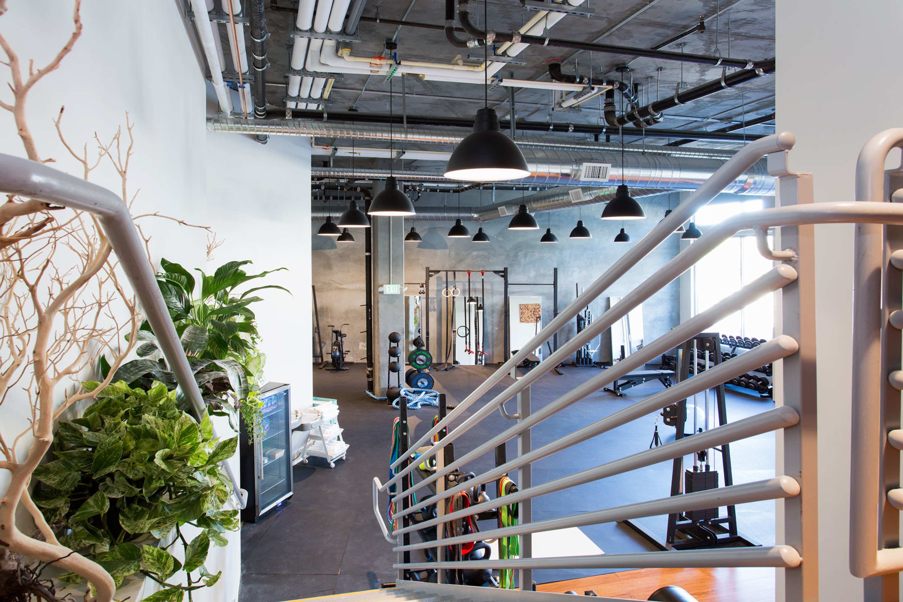 The interior of a modern gym with exercise equipment and a staircase in the foreground.