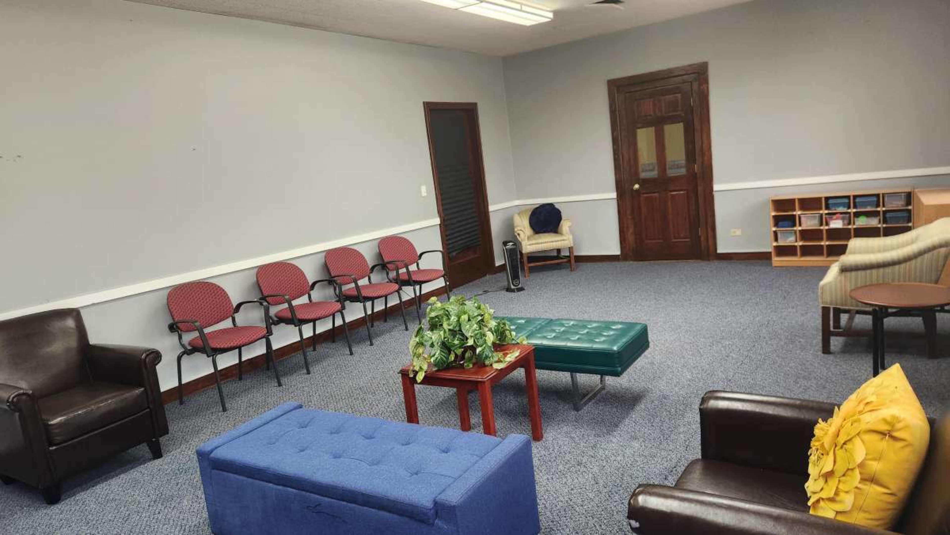 The image shows a spacious room with several chairs arranged in a semi-circle, two couches, a coffee table, and a small bookshelf against the wall.