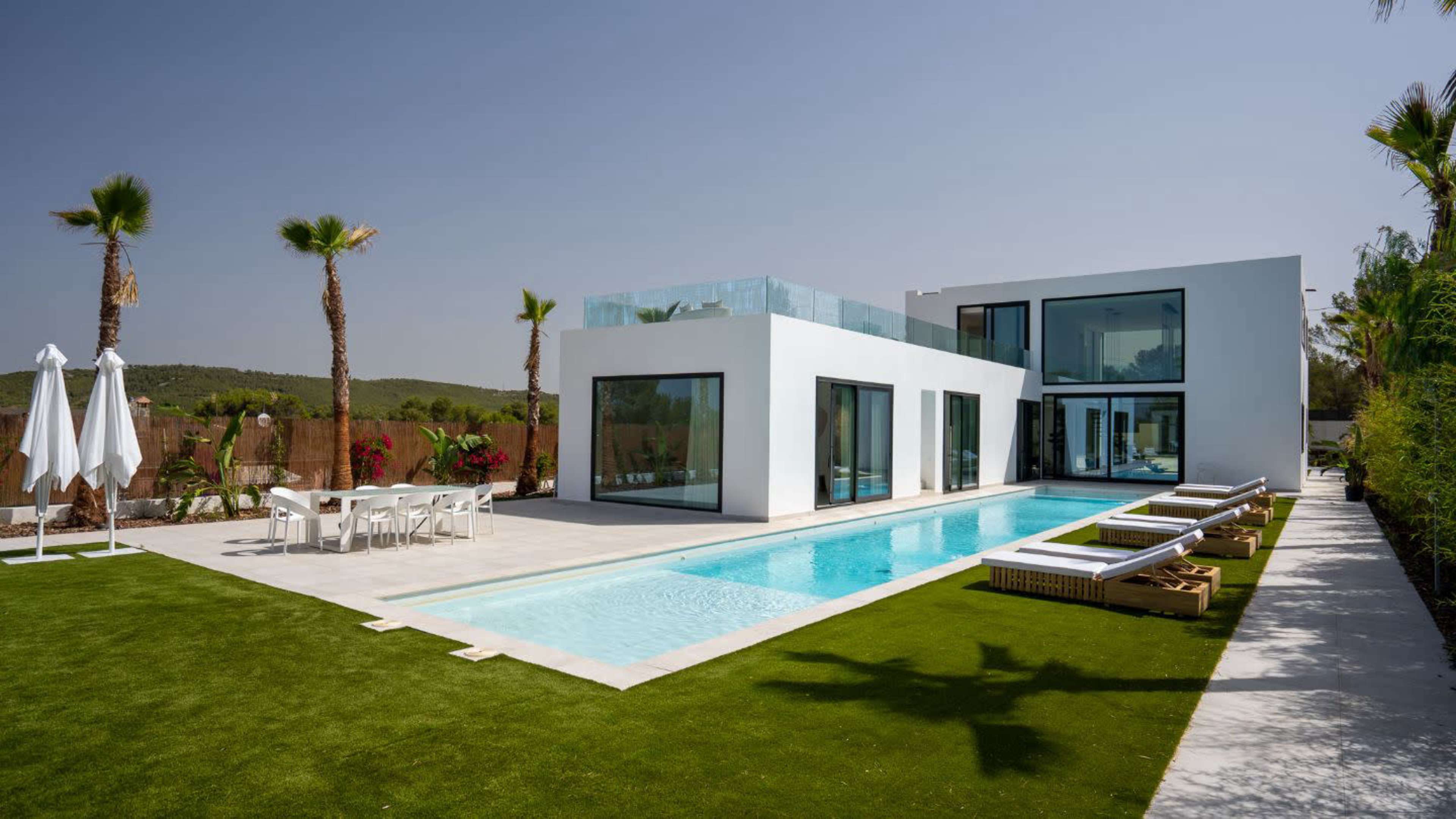 A modern house with large windows, a swimming pool, and a landscaped yard featuring palm trees and lounge chairs.