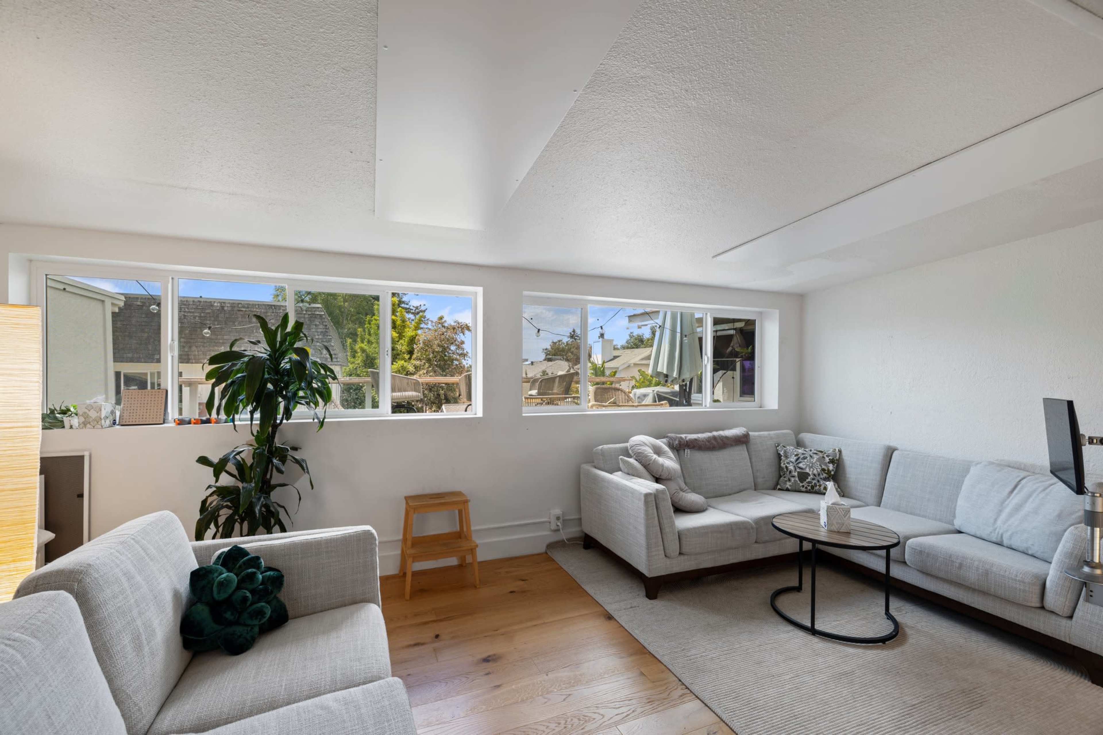 The image shows a bright, modern living room with two sofas, a small side table, and large windows allowing natural light to fill the space.