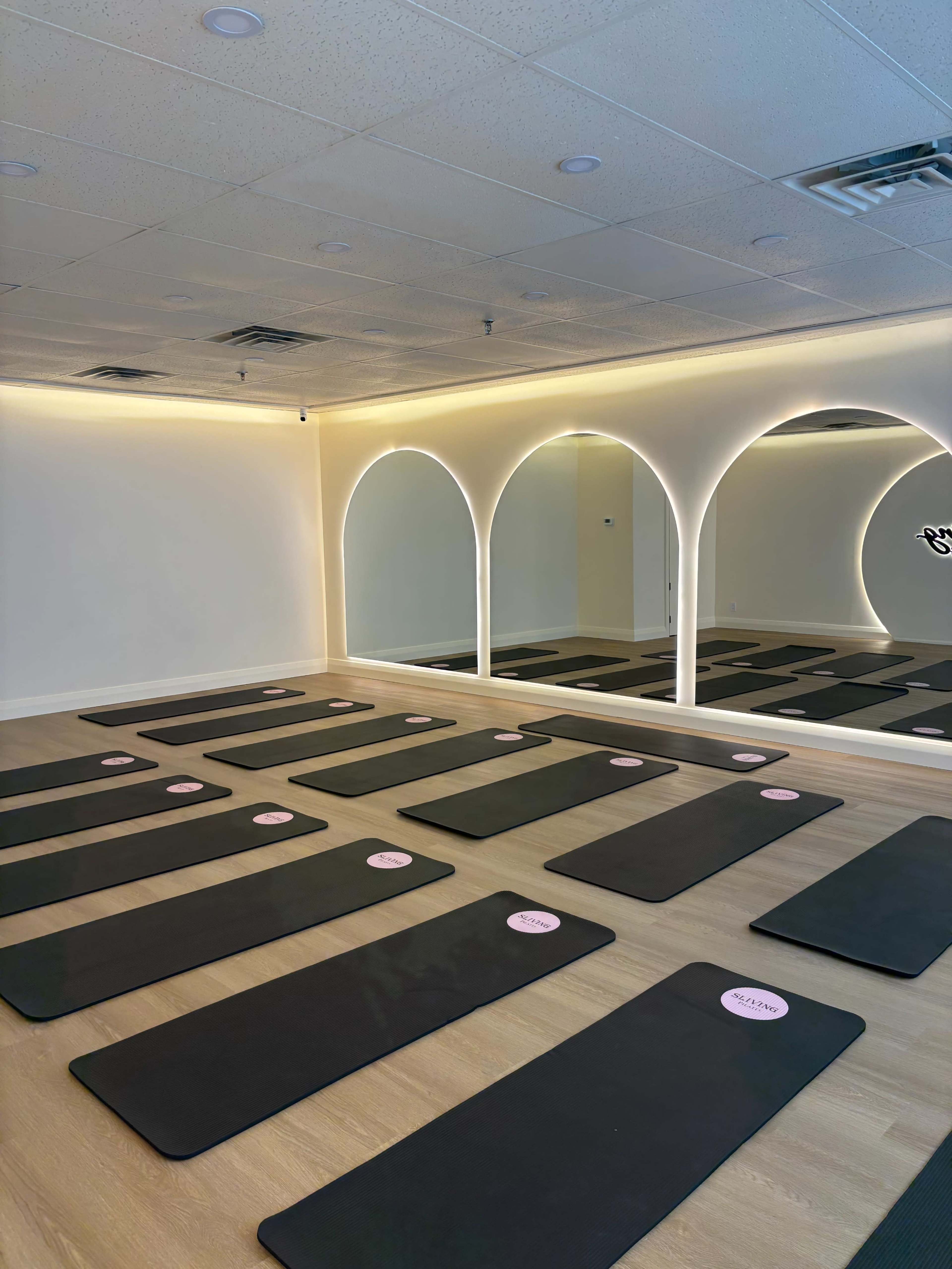 The image shows a yoga studio with several exercise mats neatly arranged on the floor in front of a large mirror framed by arches.