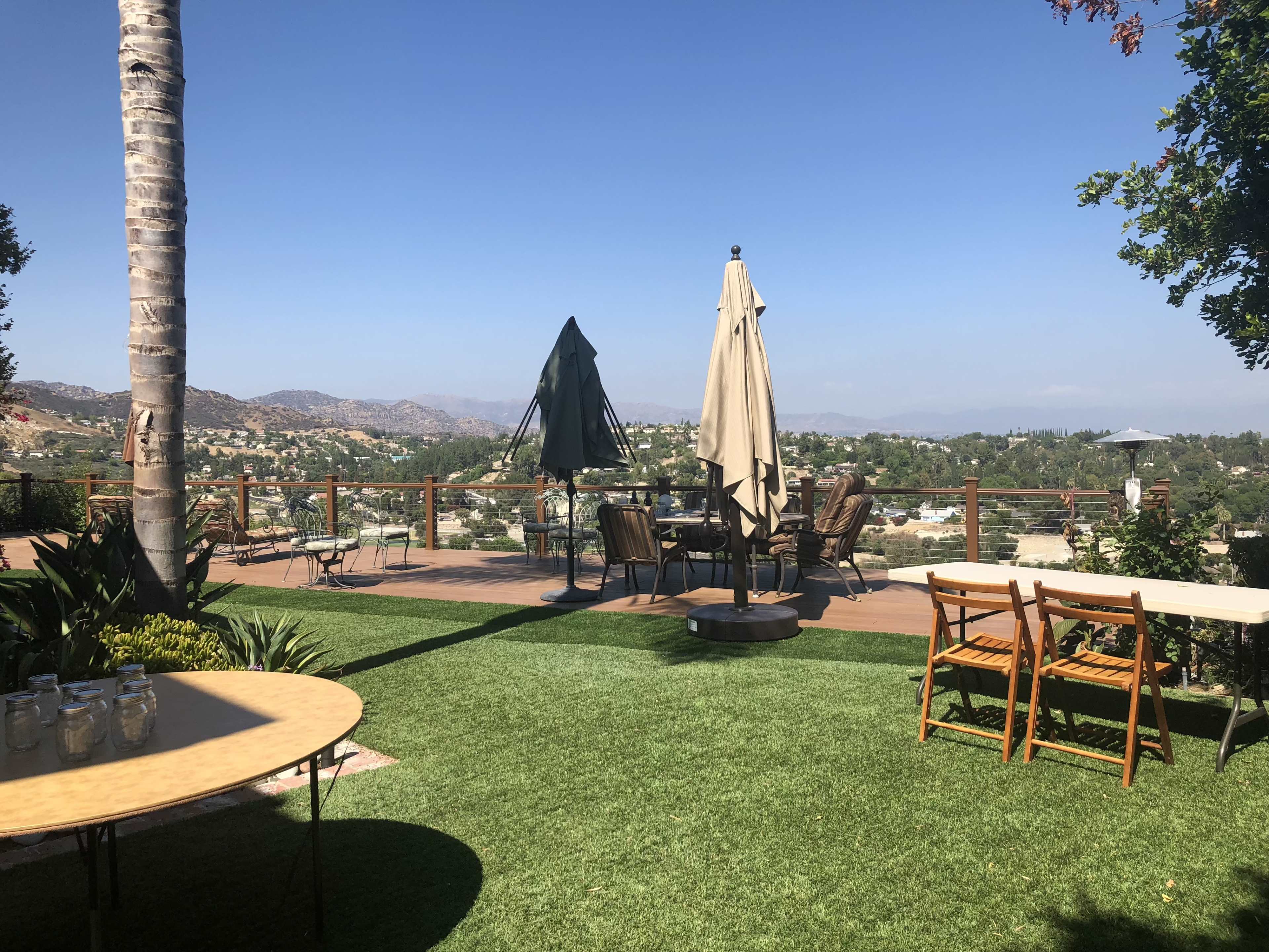 A patio area with tables, chairs, and umbrellas overlooking a valley and distant mountains.