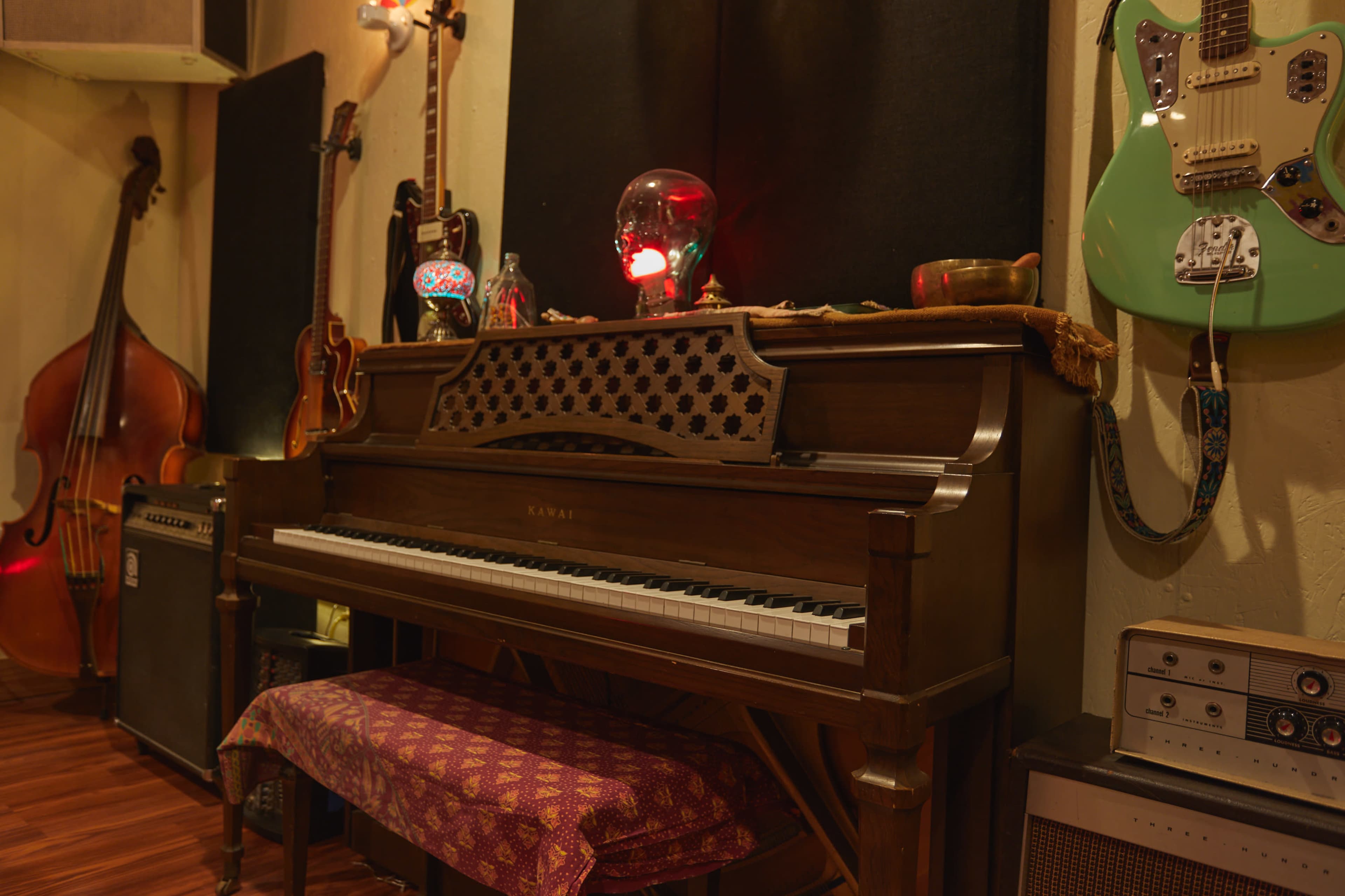 A wooden piano sits against a wall, surrounded by various musical instruments and uniquely decorated items.