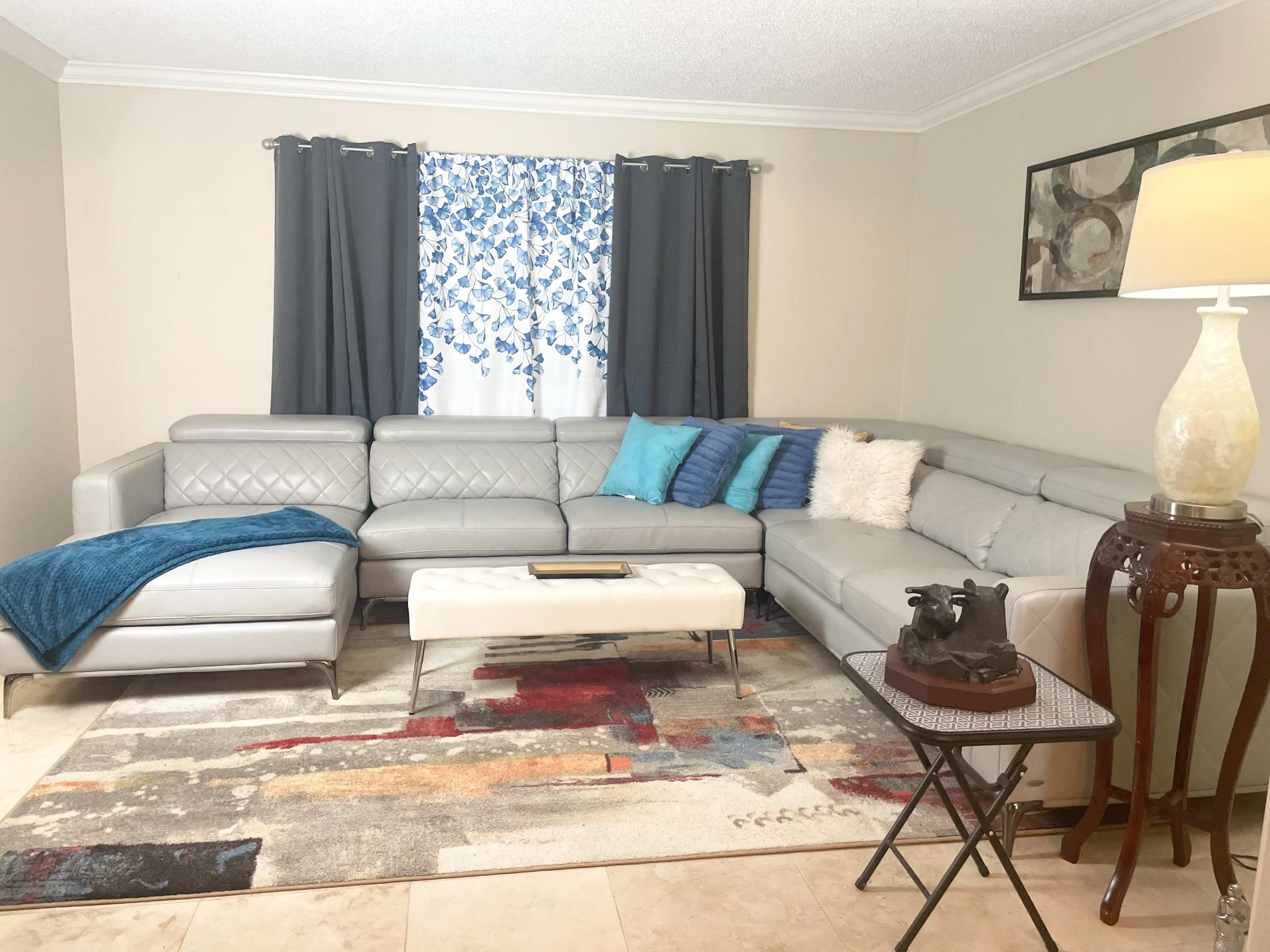 The living room features a gray sectional sofa, a decorative rug with colorful patterns, and a small side table beside a lamp.