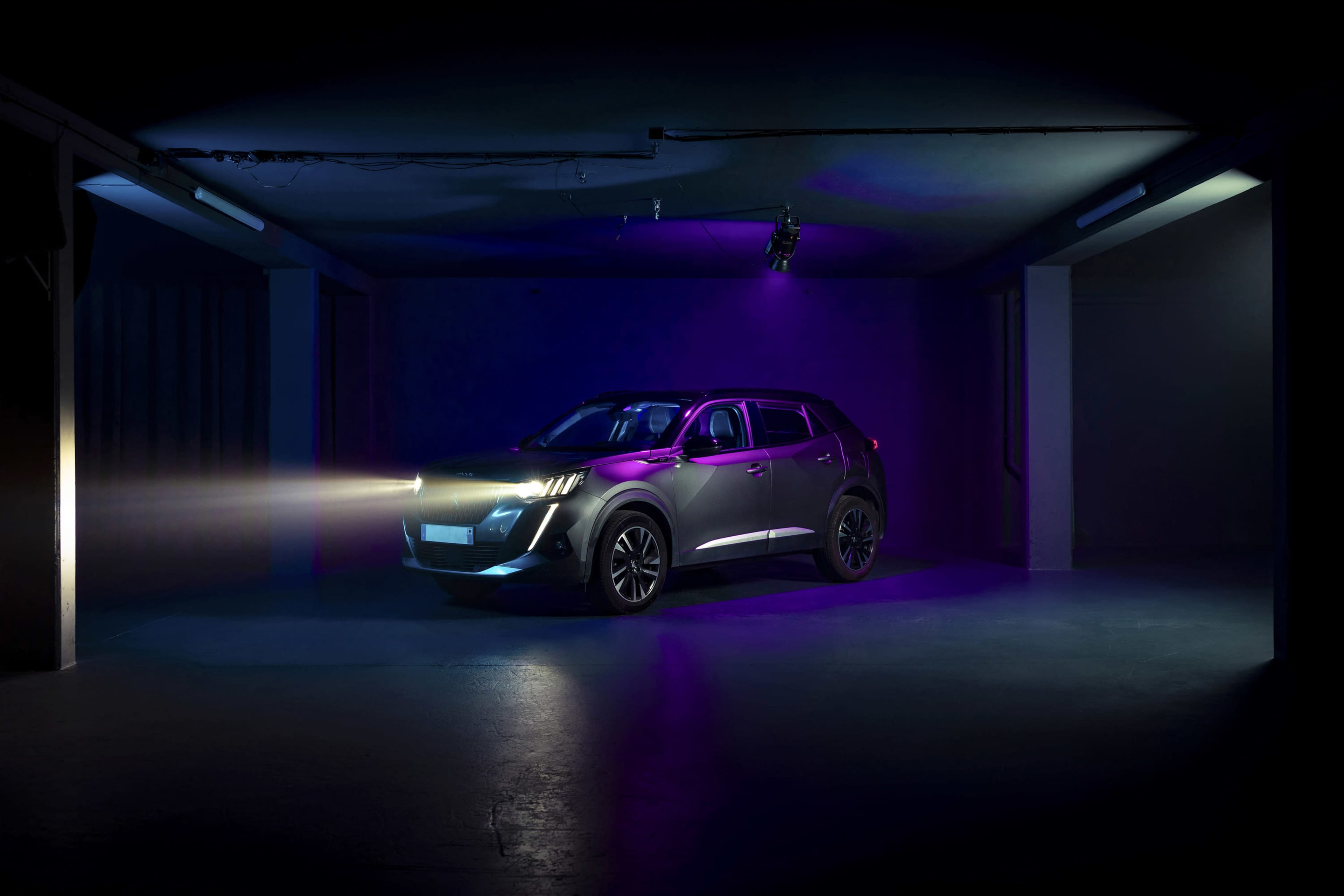 A modern SUV is illuminated by its headlights in a dimly lit room with colorful lighting.