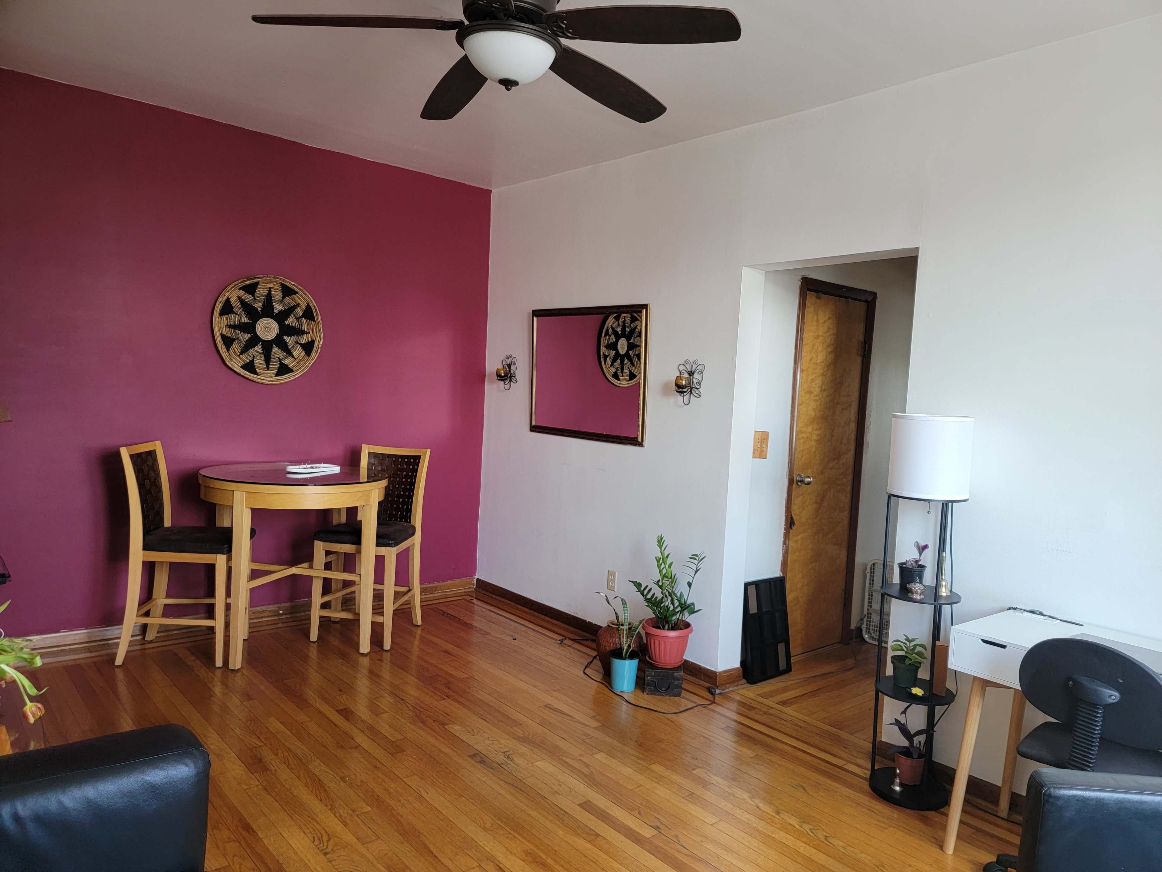 A room with hardwood floors, a round wooden dining table with two chairs, a pink accent wall, and a doorway leading to another space.