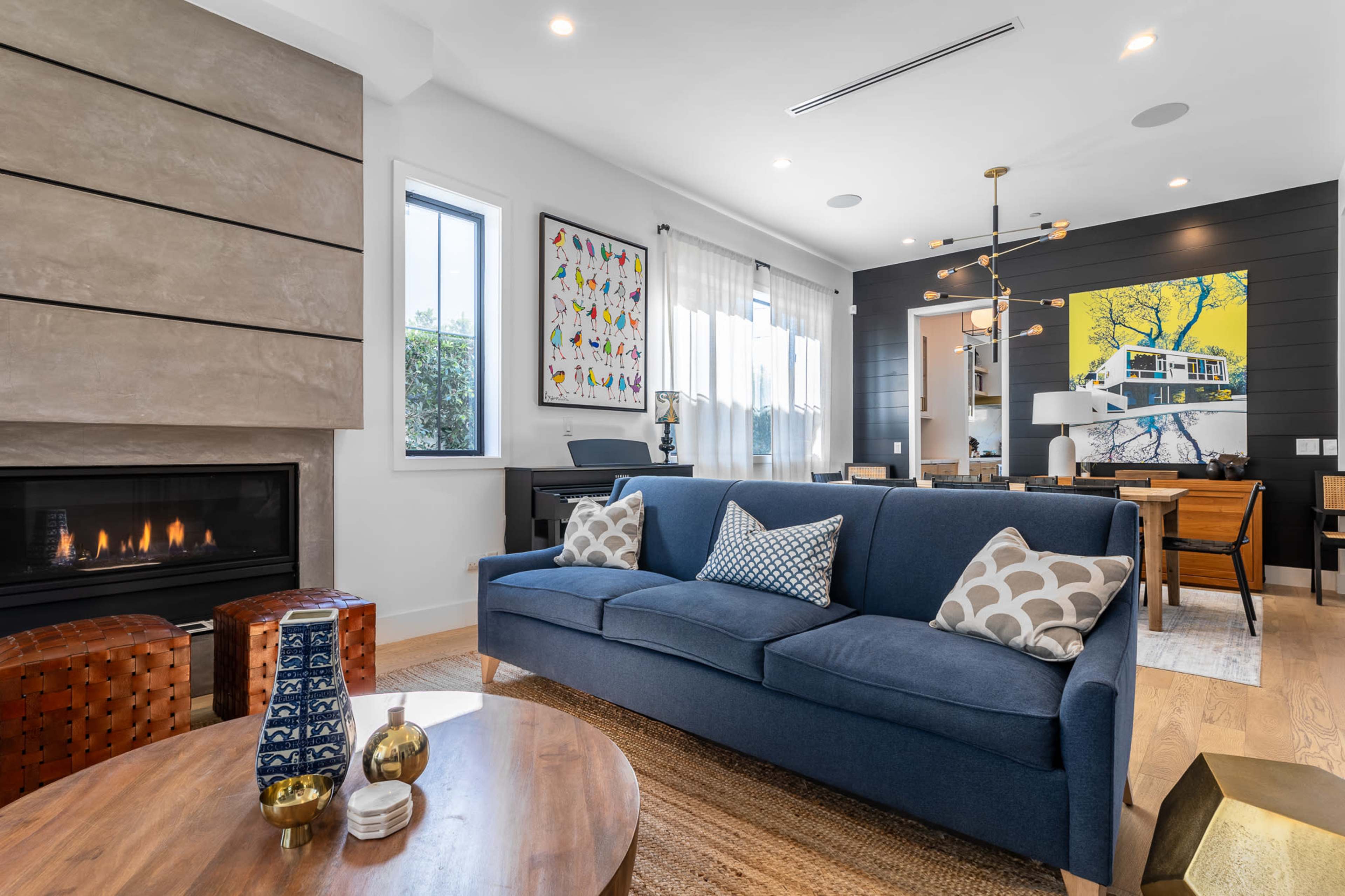 A modern living room features a blue sofa, geometric decor, a cozy fireplace, and artwork on the walls.