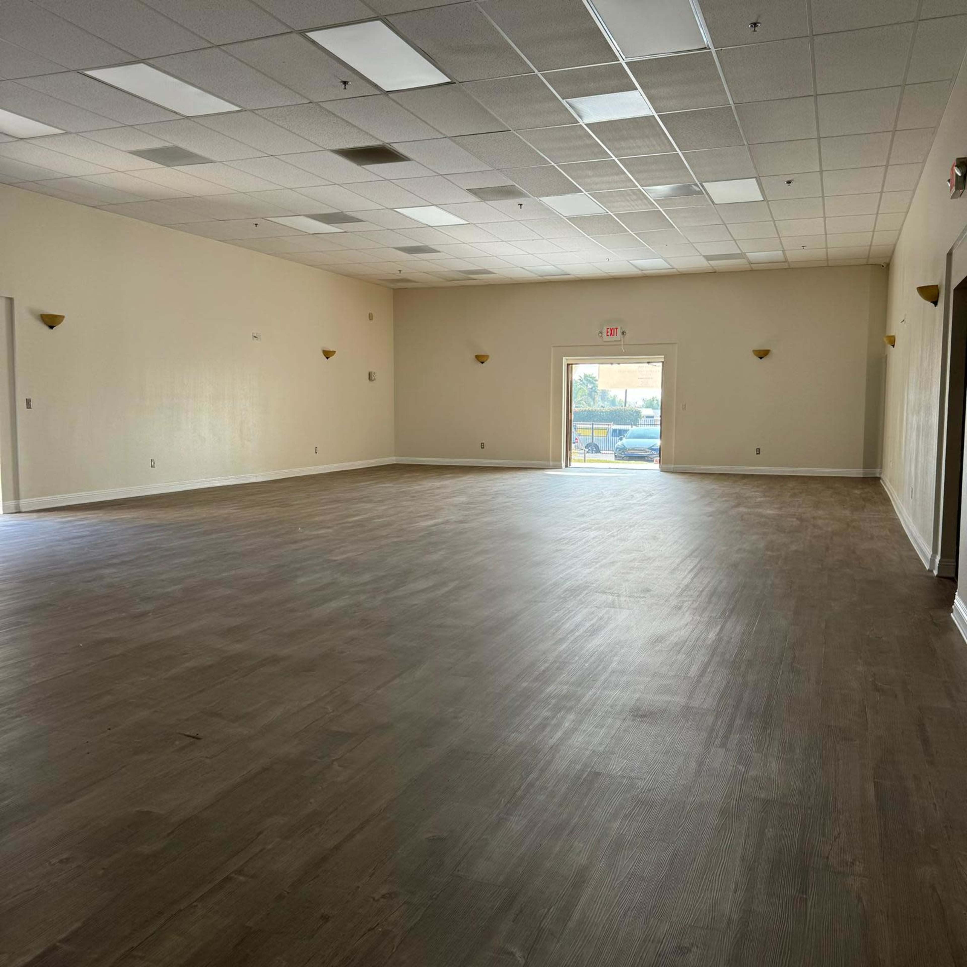 A spacious, empty room with light-colored walls and a single door leading to an outdoor area.