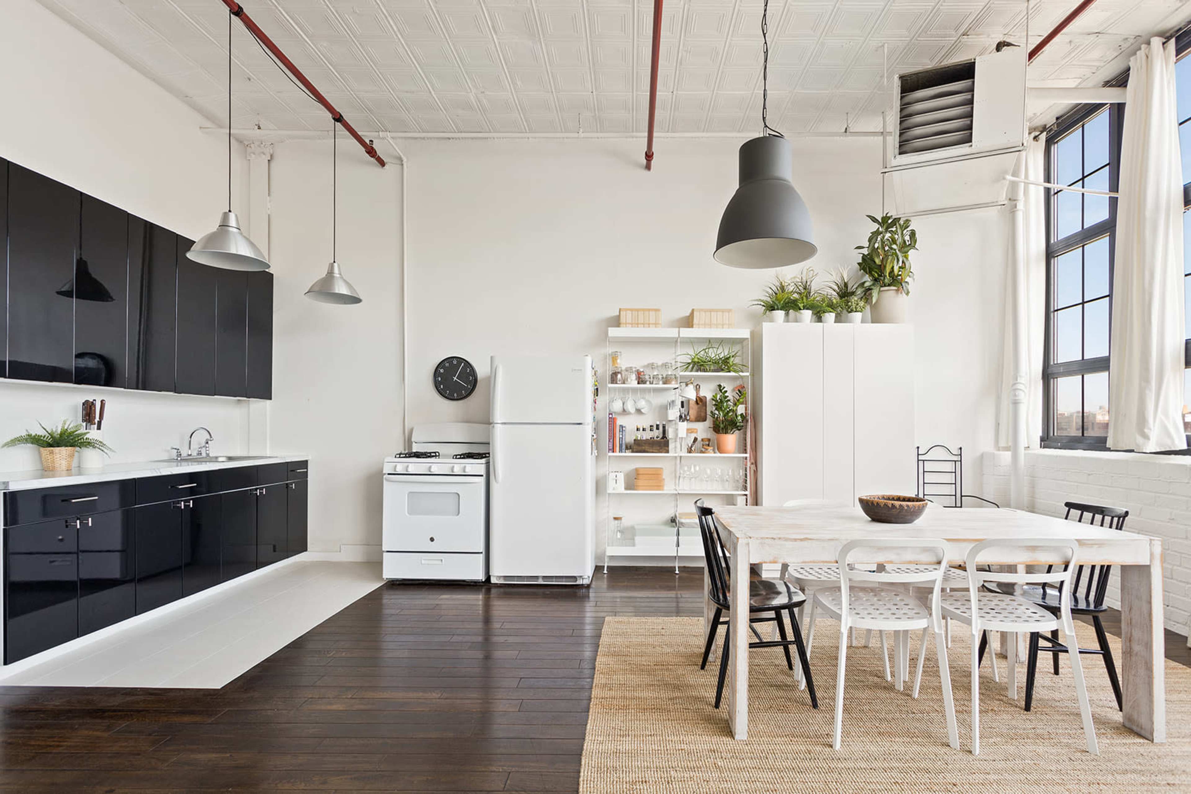 A modern kitchen with black cabinetry, a white stove, and a dining area featuring a large wooden table surrounded by black and white chairs.
