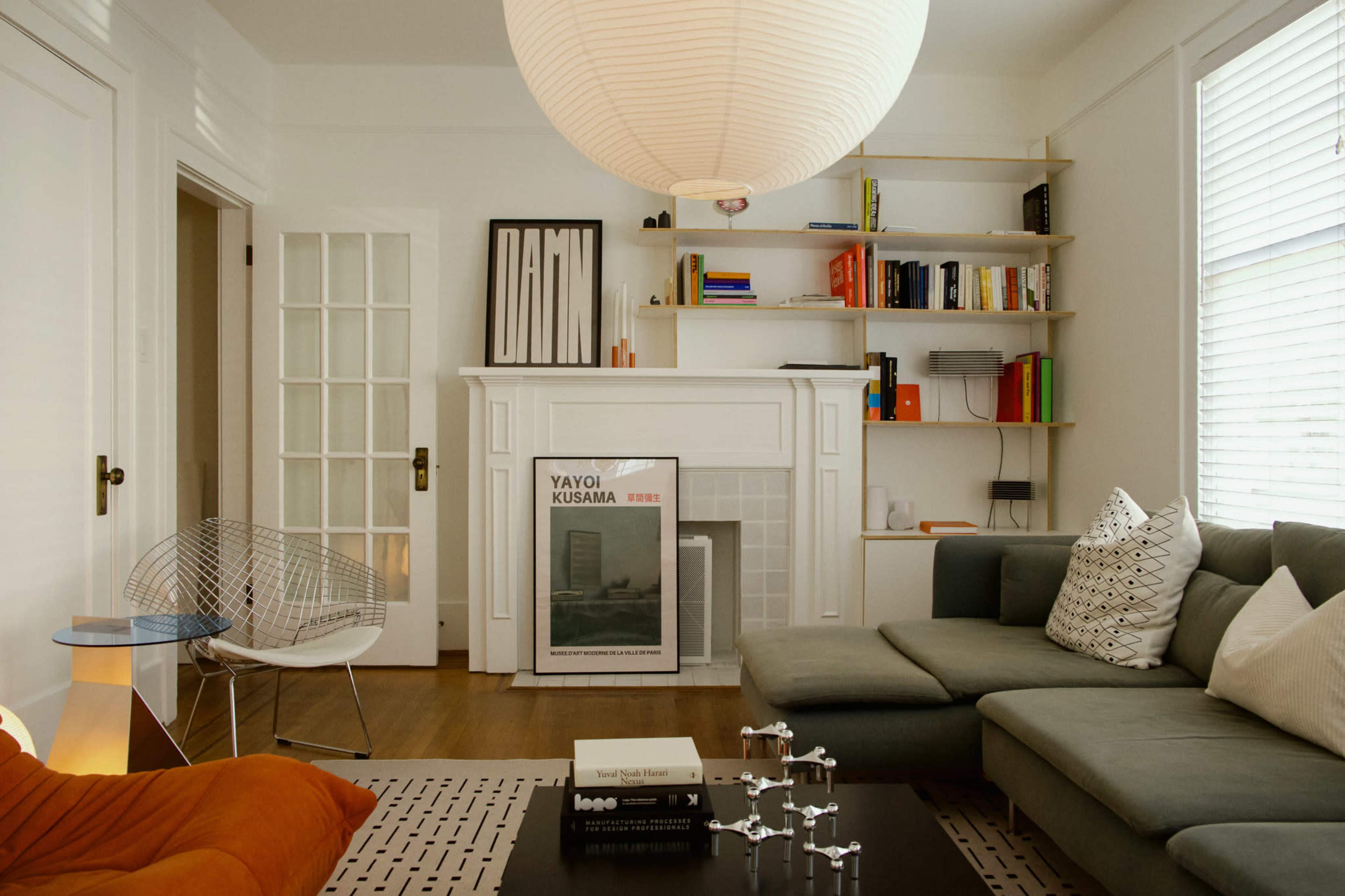 The image shows a modern living room with a sectional sofa, a light fixture, shelves filled with books, and a decorative fireplace.