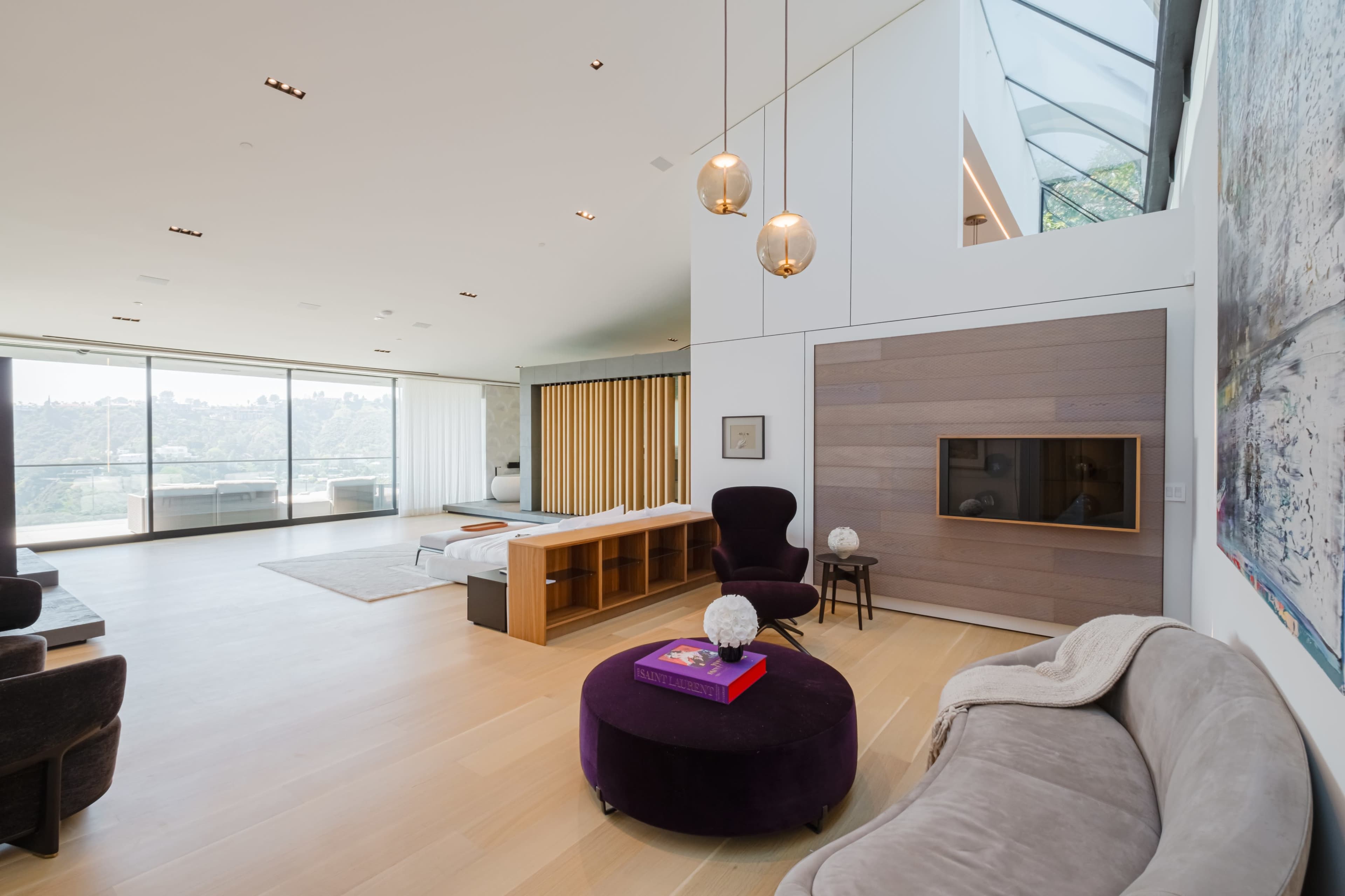 A modern living space with large windows, a plush seating area, and a minimalist design featuring light wood flooring.