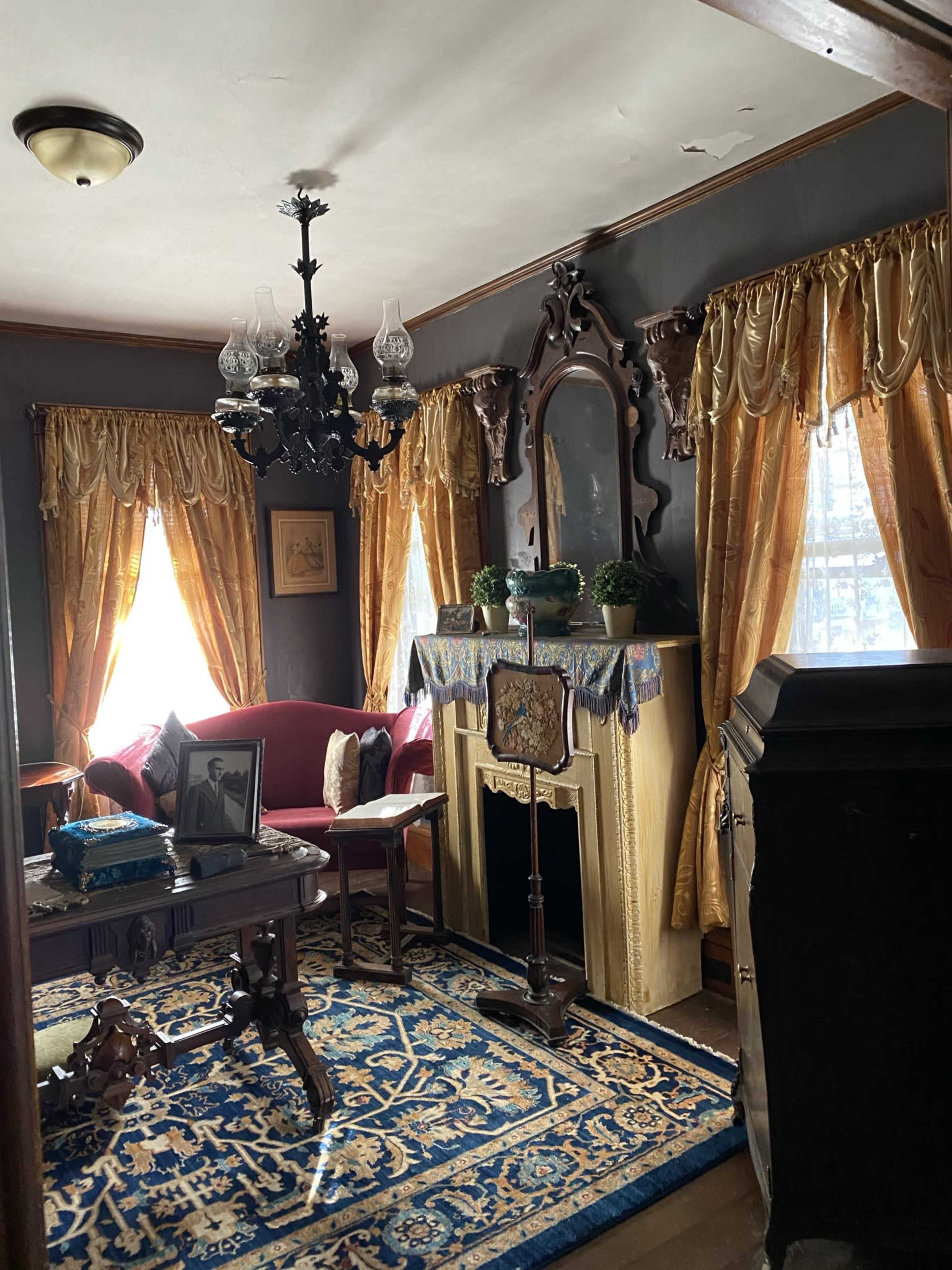 The room features a red velvet sofa, ornate curtains, a vintage chandelier, and a decorative fireplace with plants on the mantel.
