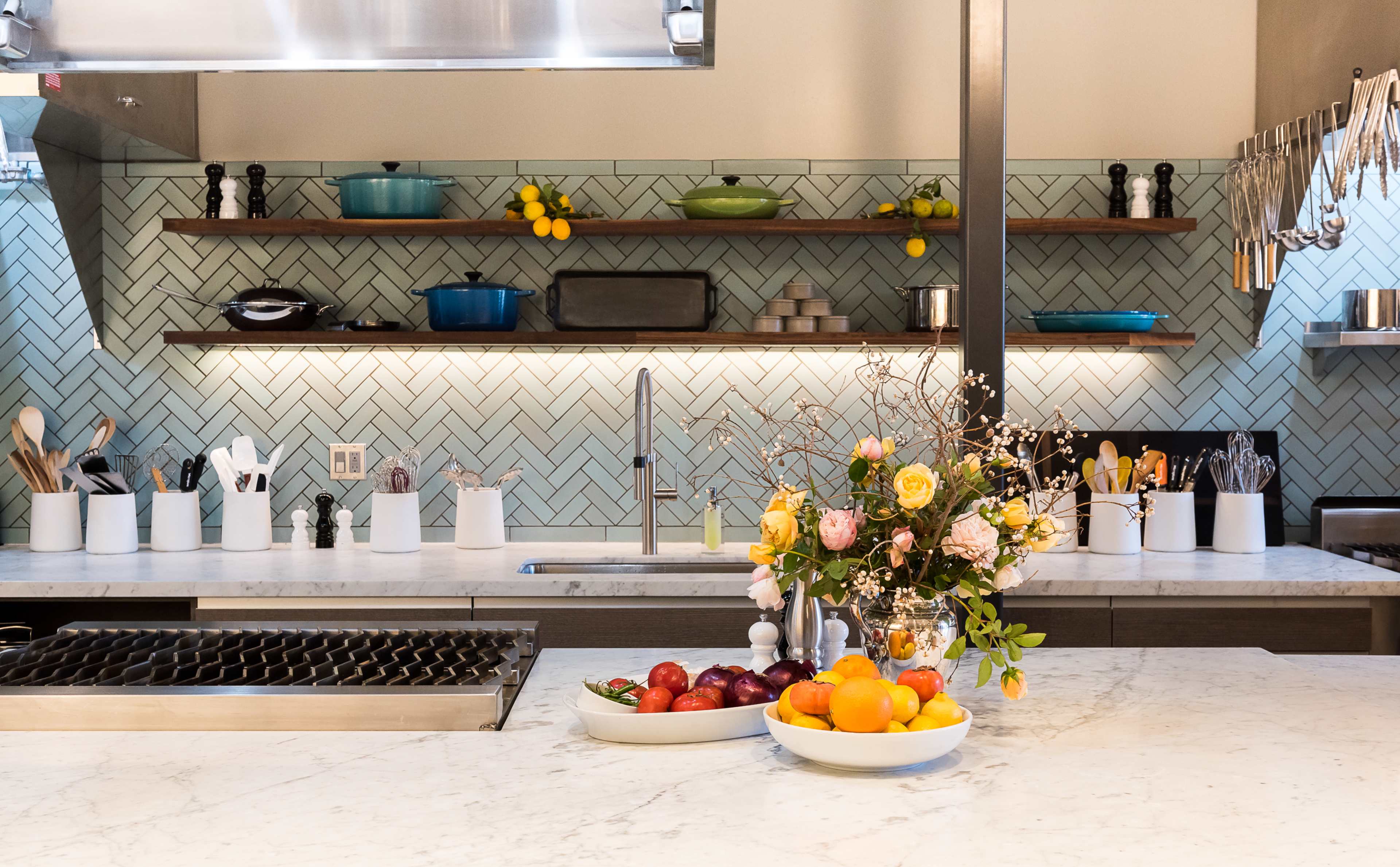 A modern kitchen features a marble countertop, a herringbone backsplash in shades of green, and shelves displaying cookware and decorative items.