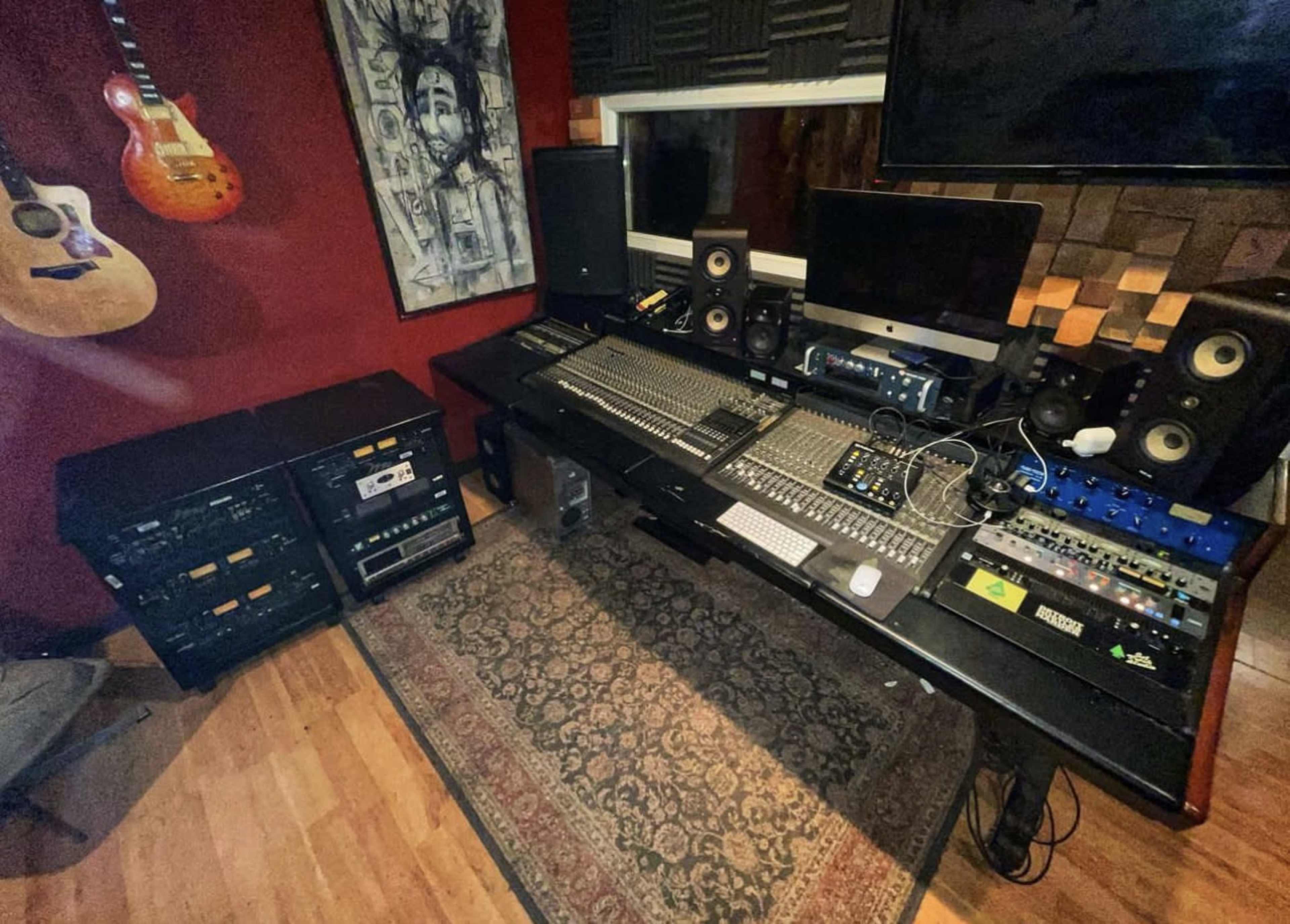 A music production studio with a large mixing console, audio equipment, and guitars hanging on the wall.