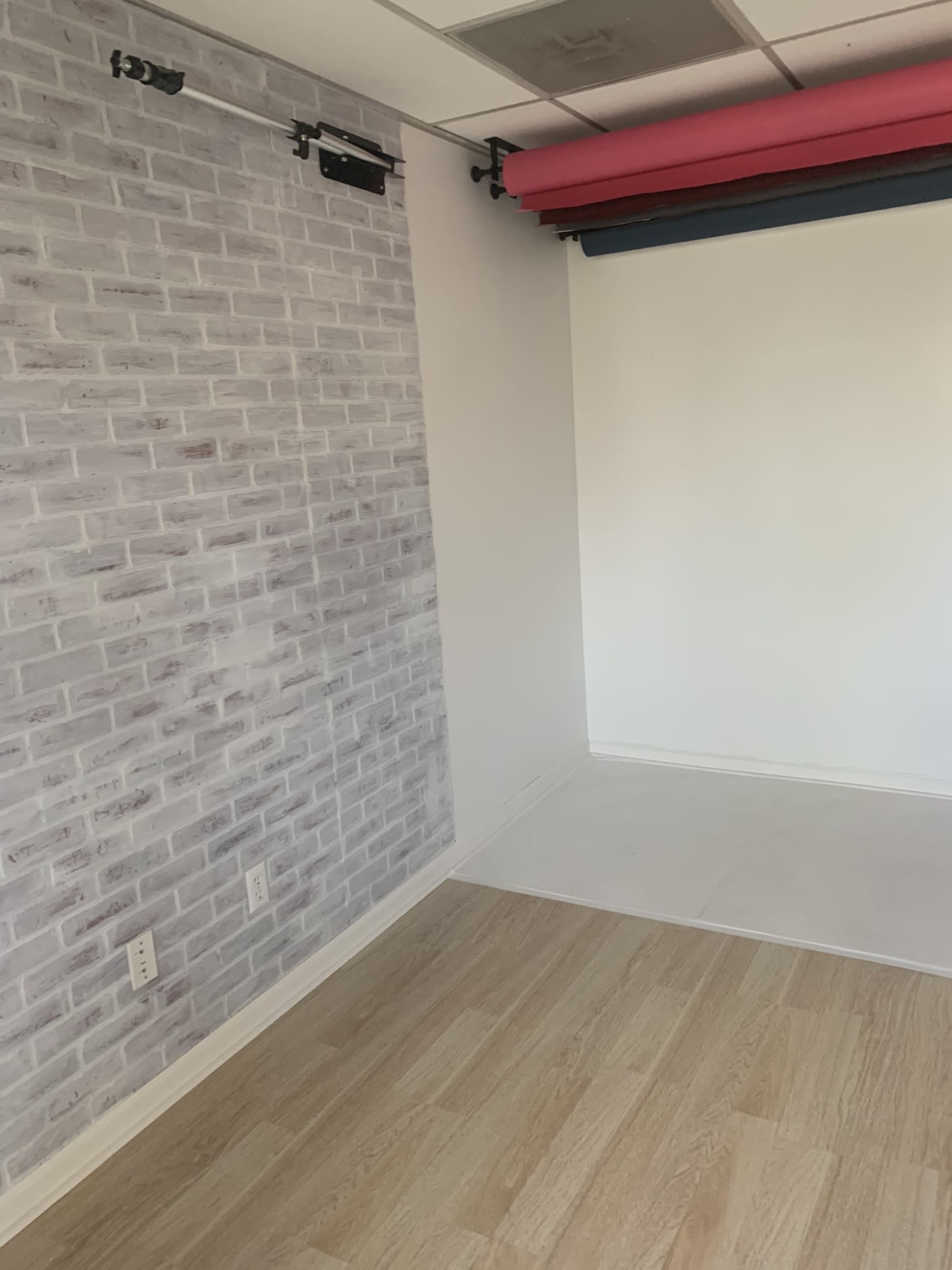 A room with a brick-patterned wall on one side, a plain white wall on the other, and a light wooden floor.