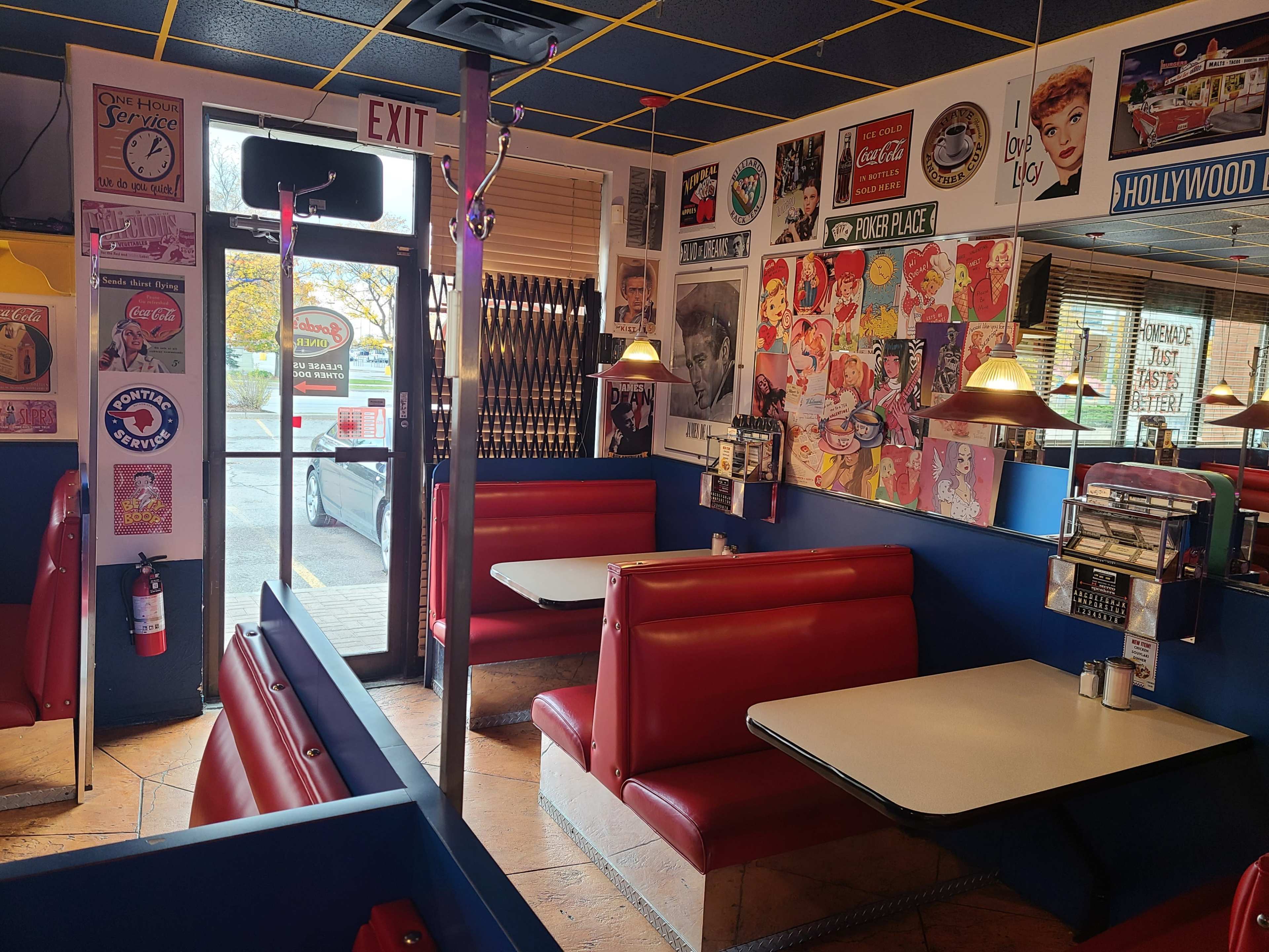 The image shows the interior of a diner featuring red vinyl booths, a table in the center, and vintage advertisements on the walls.