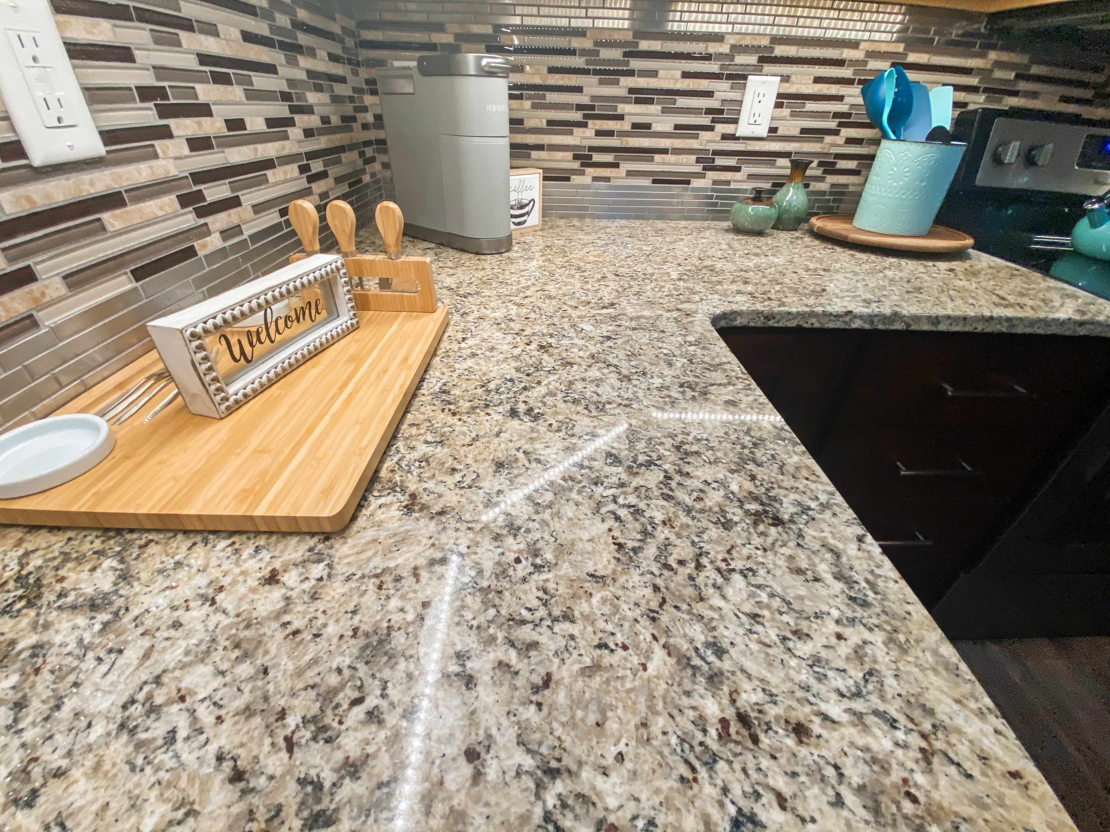 A kitchen countertop made of speckled granite, with a wooden tray that displays a "Welcome" sign and several kitchen utensils.