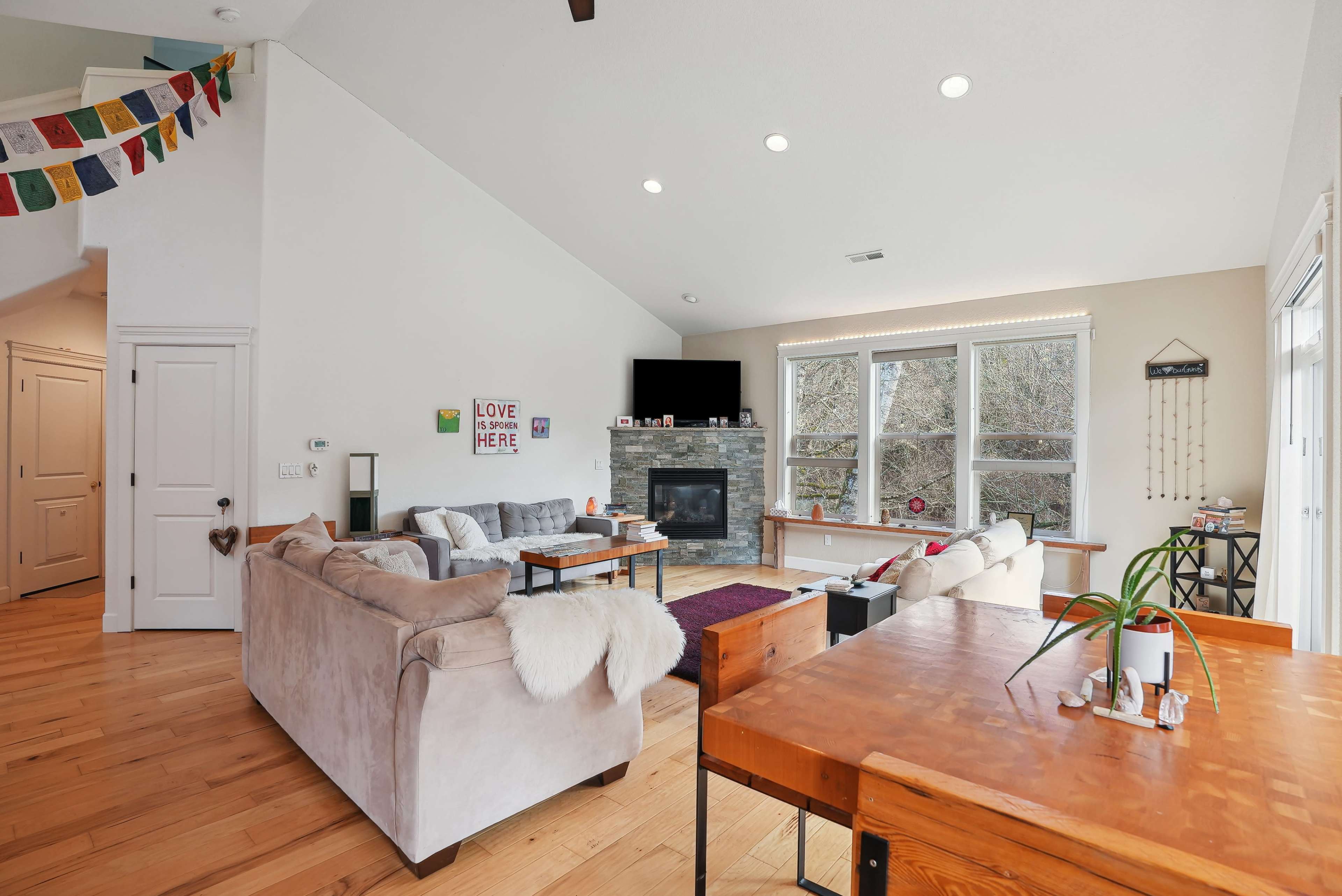 The living area features a sofa and coffee table, a fireplace, and large windows, with a dining table visible in the foreground.