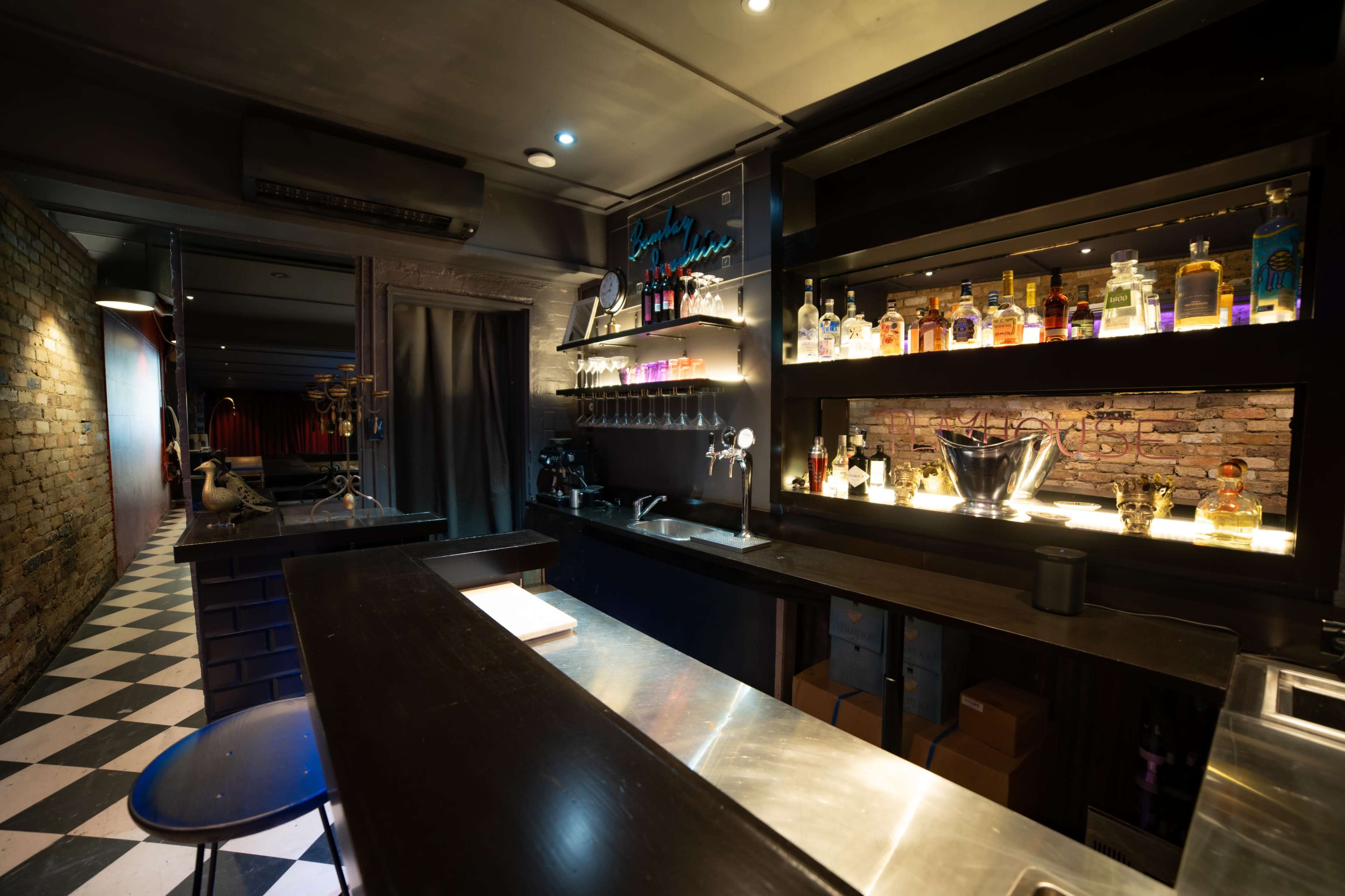 The image shows a dimly lit bar with a polished countertop, shelves displaying various bottles, and a black-and-white checkered floor.