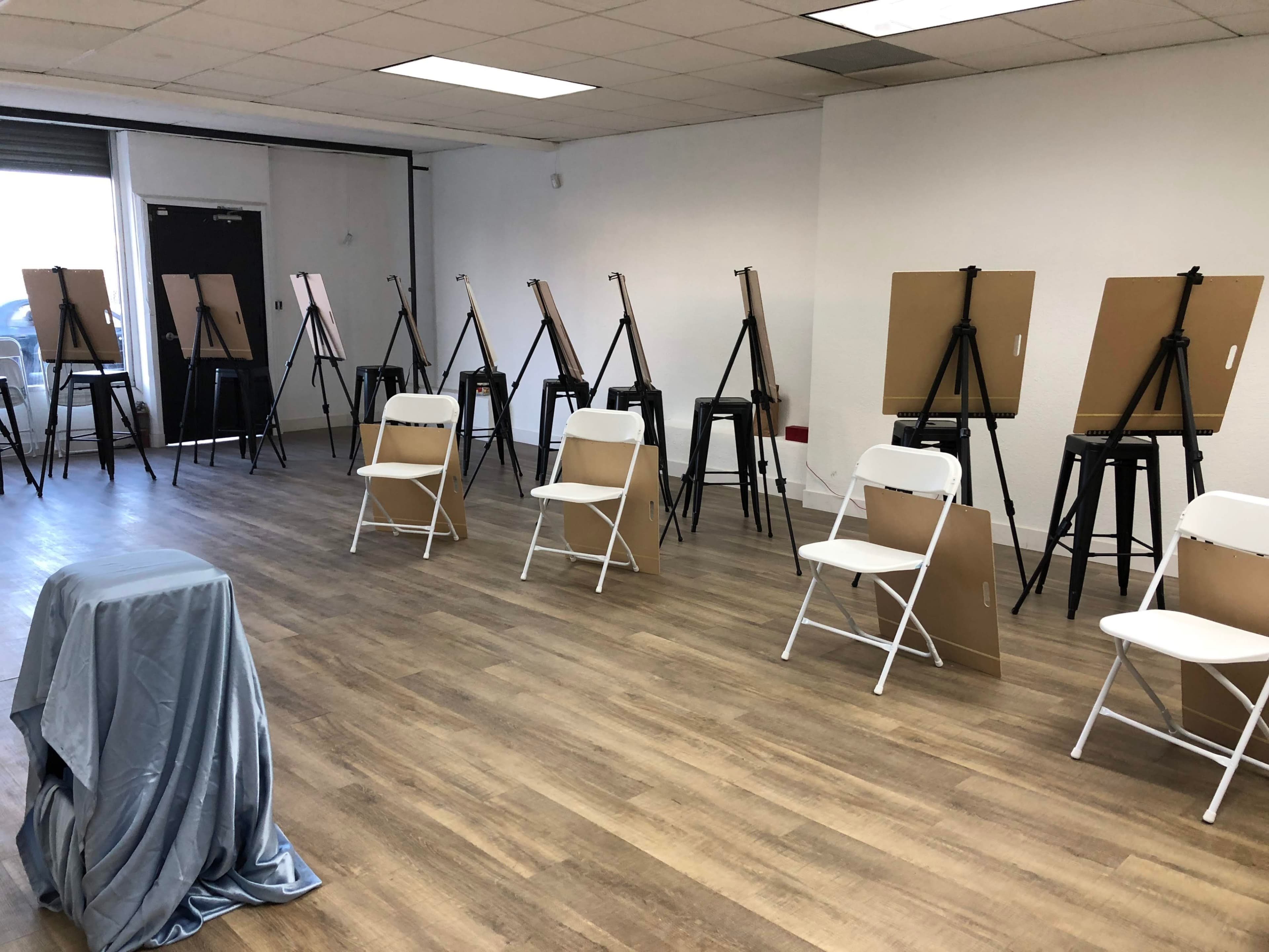 An empty art studio with multiple easels and chairs arranged in a spacious room with wooden flooring.
