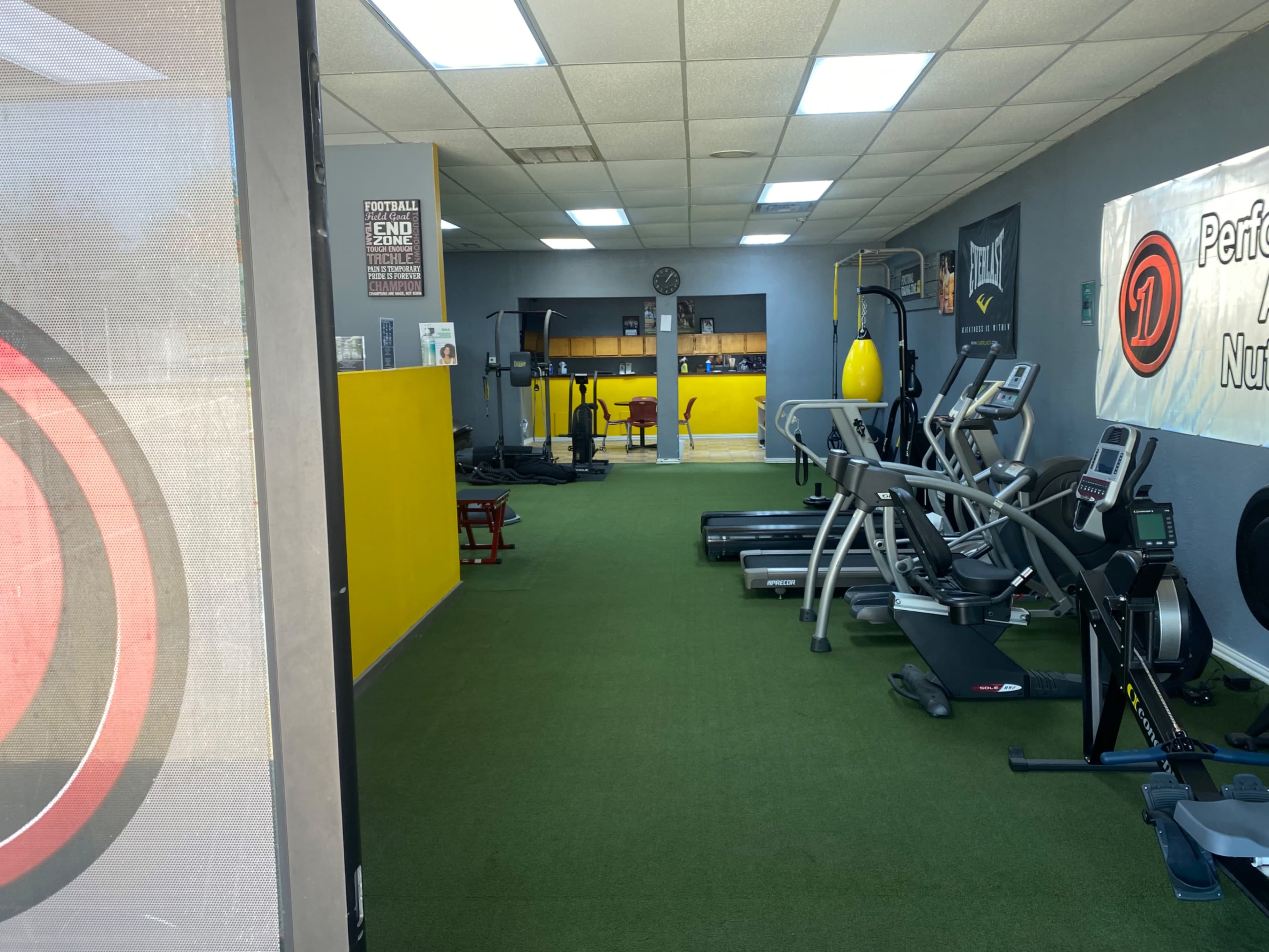 A gym interior with various exercise equipment, including treadmills, stationary bikes, and weight machines, set against a green carpeted floor.