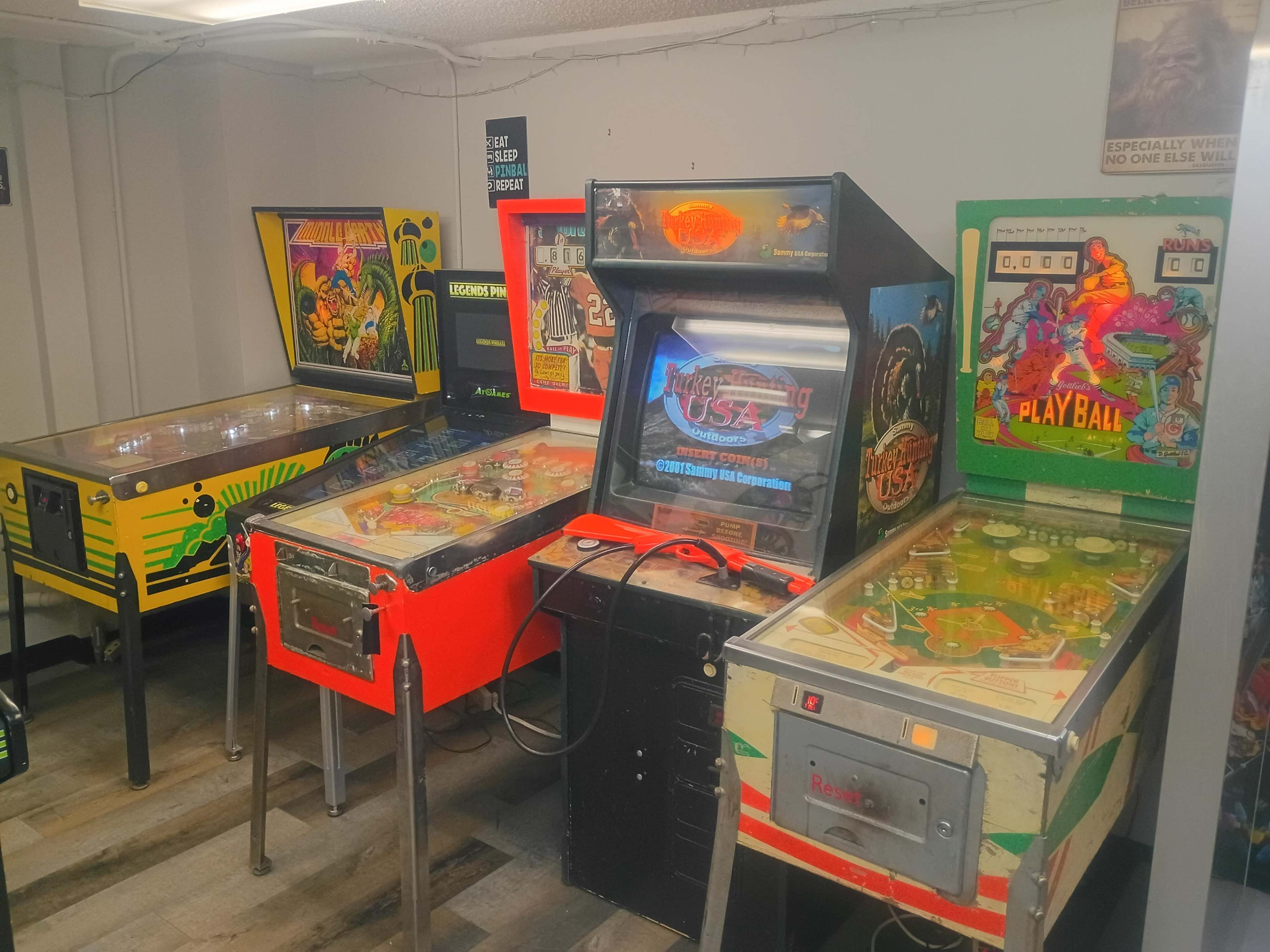 The image shows a corner of a room featuring four vintage pinball machines, each with distinct designs and colors.