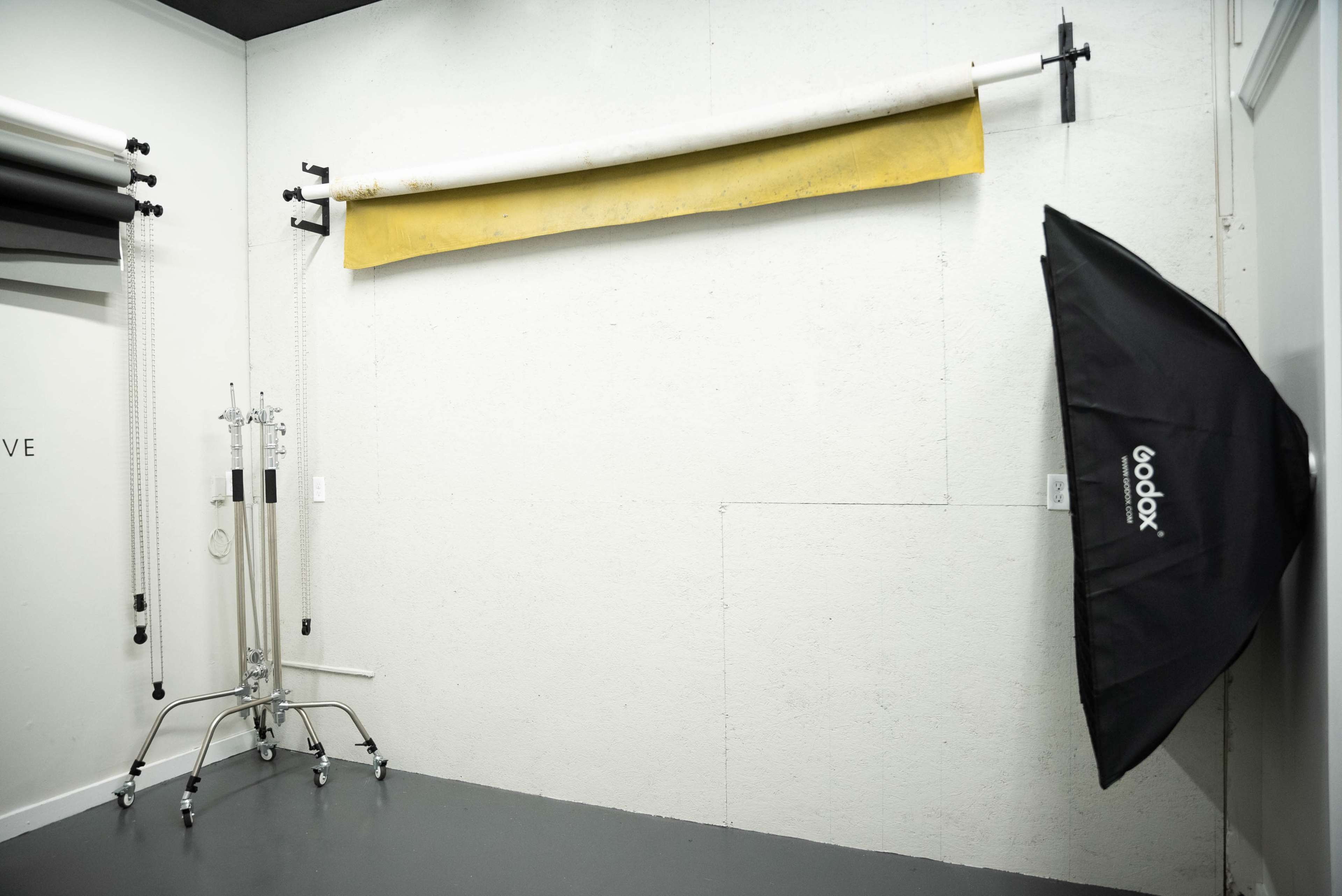 A photography studio with a yellow backdrop hanging on the wall and a Godox softbox on a stand in the corner.