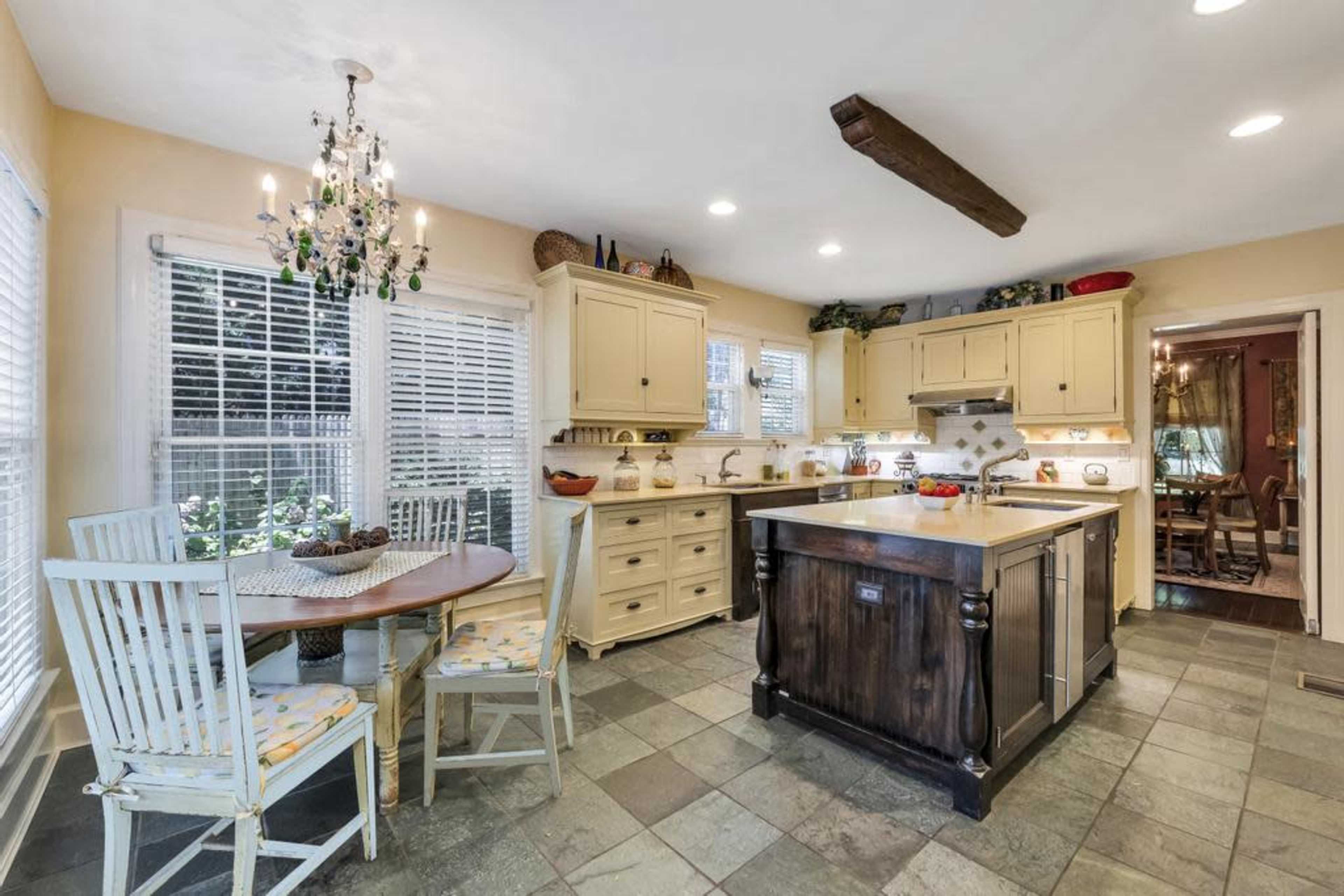 A spacious kitchen with cream-colored cabinets, a central dark wood island, and a dining table with four chairs near large windows.