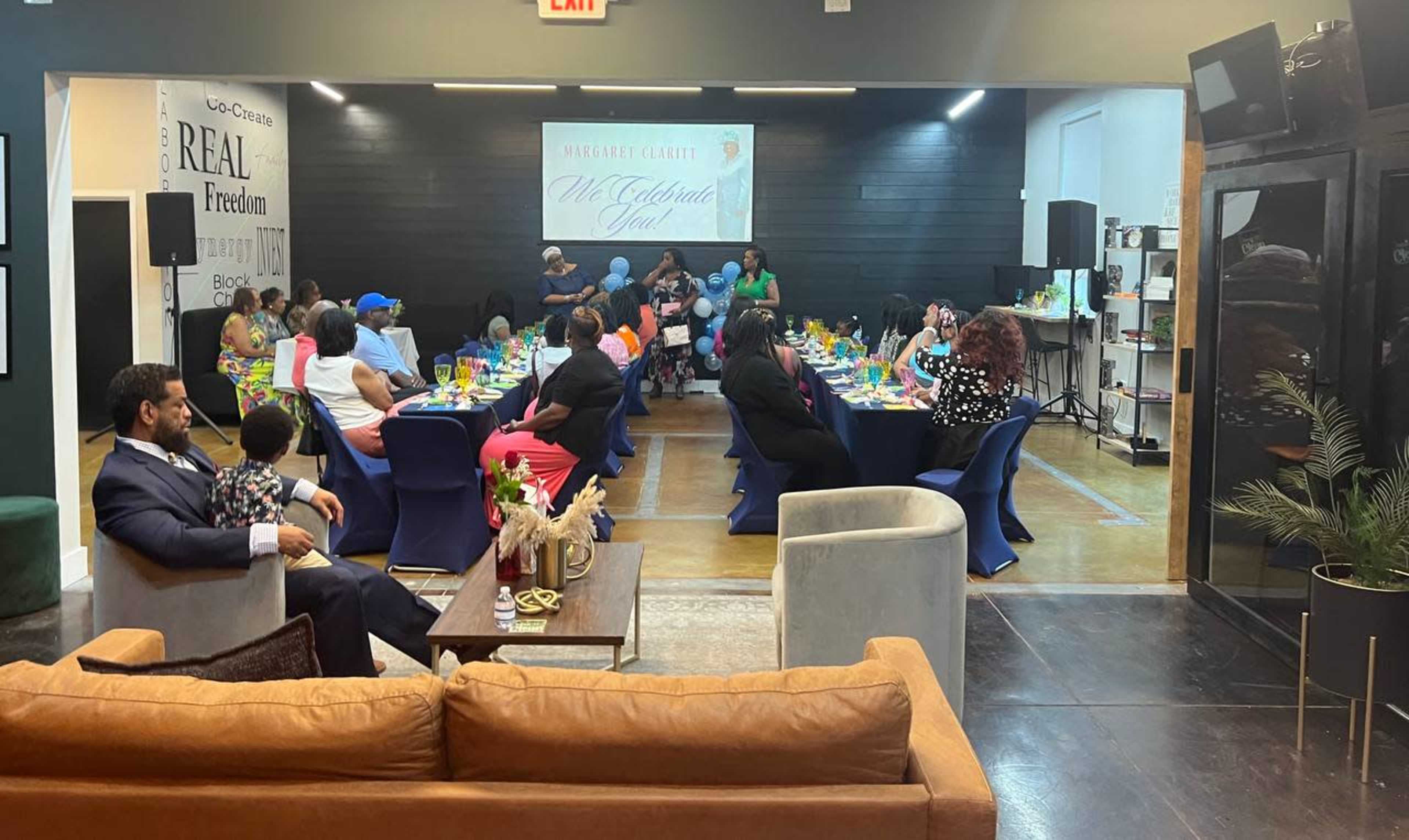 A group of people gathers around a long table decorated with colorful drinks and tableware in a well-lit event space.
