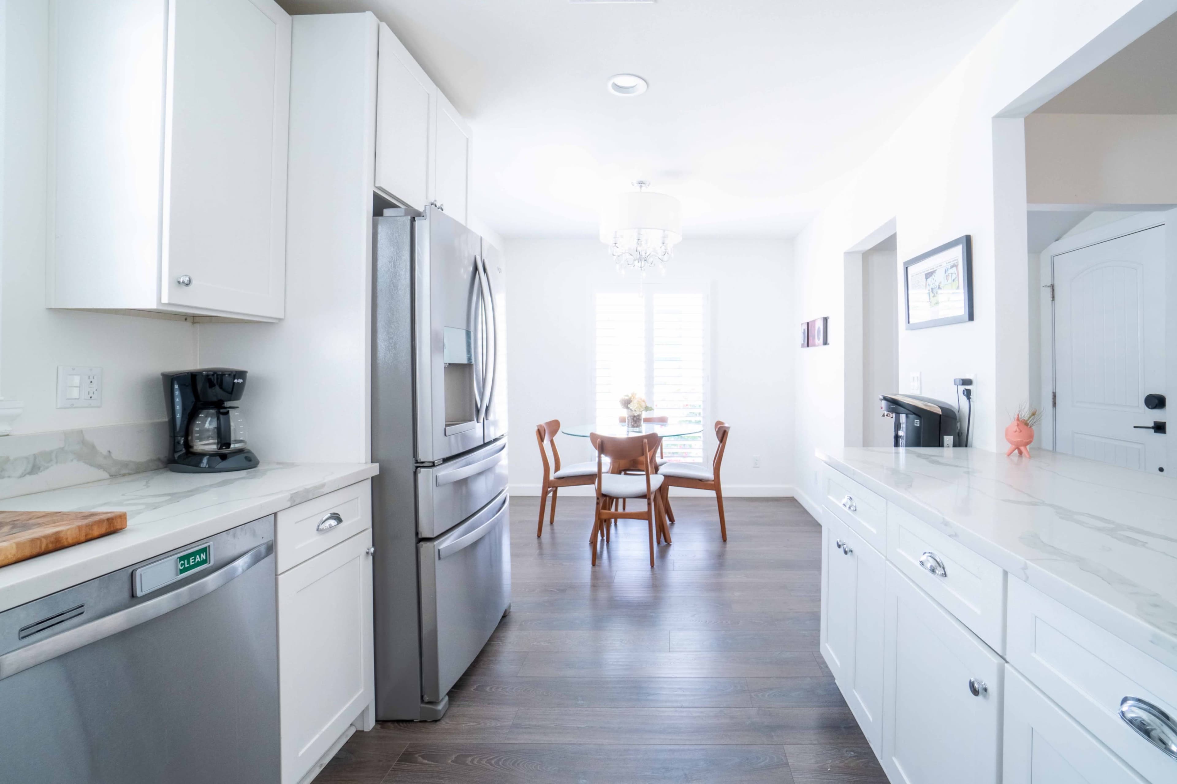 A modern kitchen features stainless steel appliances, wooden cabinets, and a dining table with chairs visible through a doorway.
