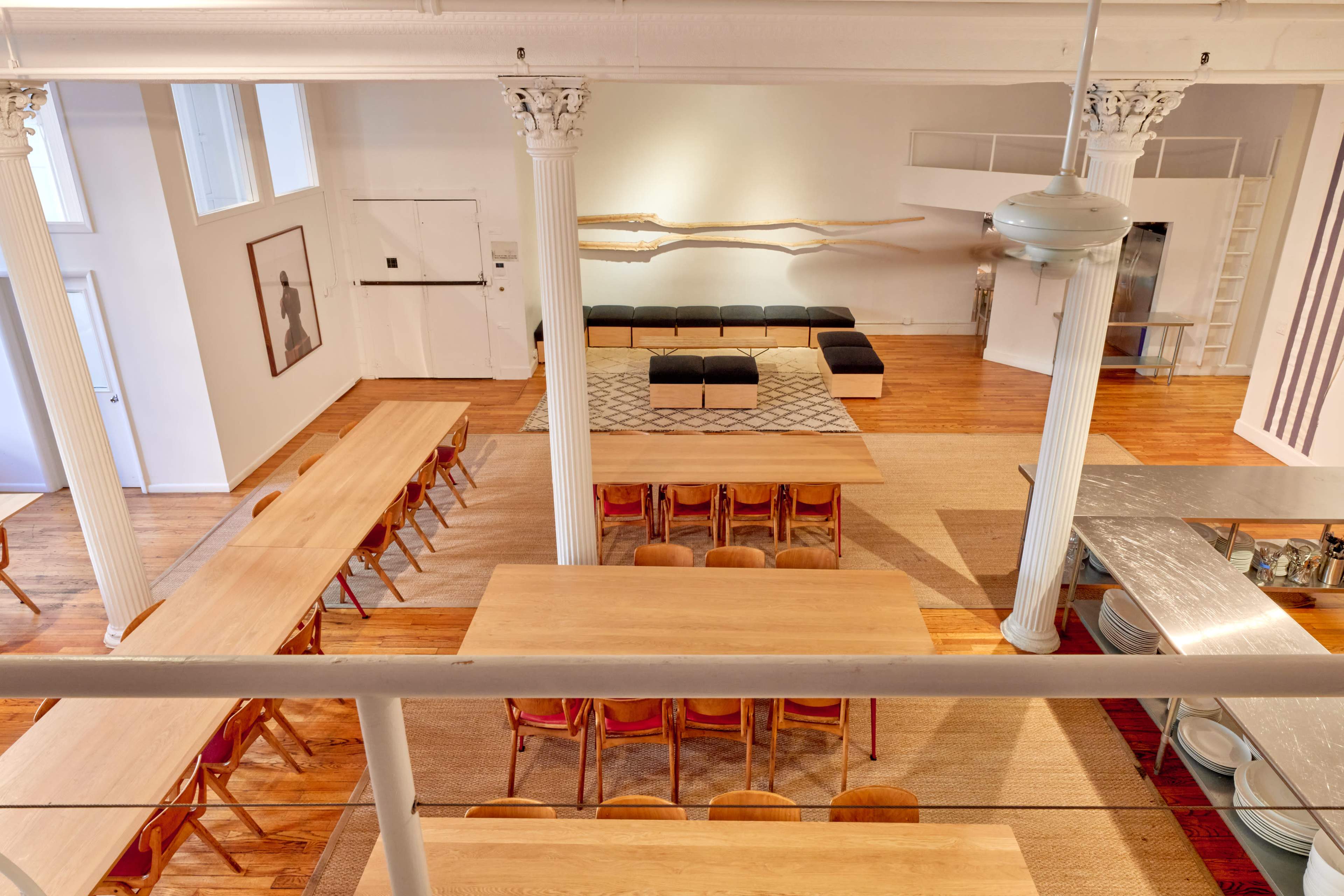 The image shows a spacious, modern interior of a dining area with multiple long tables, seating, and a decorative wall feature.