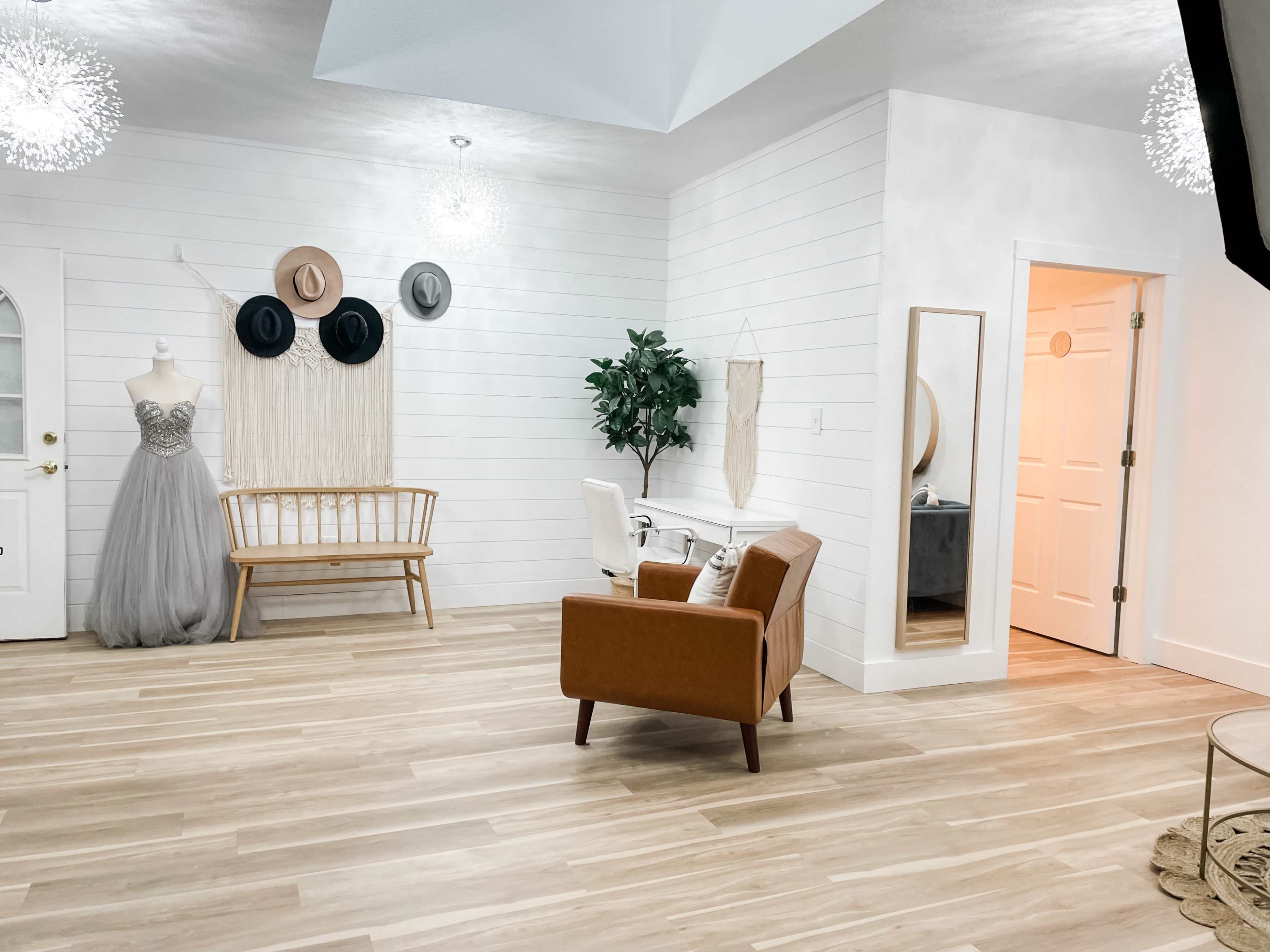 The room features light wood flooring, a bench, a dress form with a gown, two armchairs, and a doorway leading to another space.