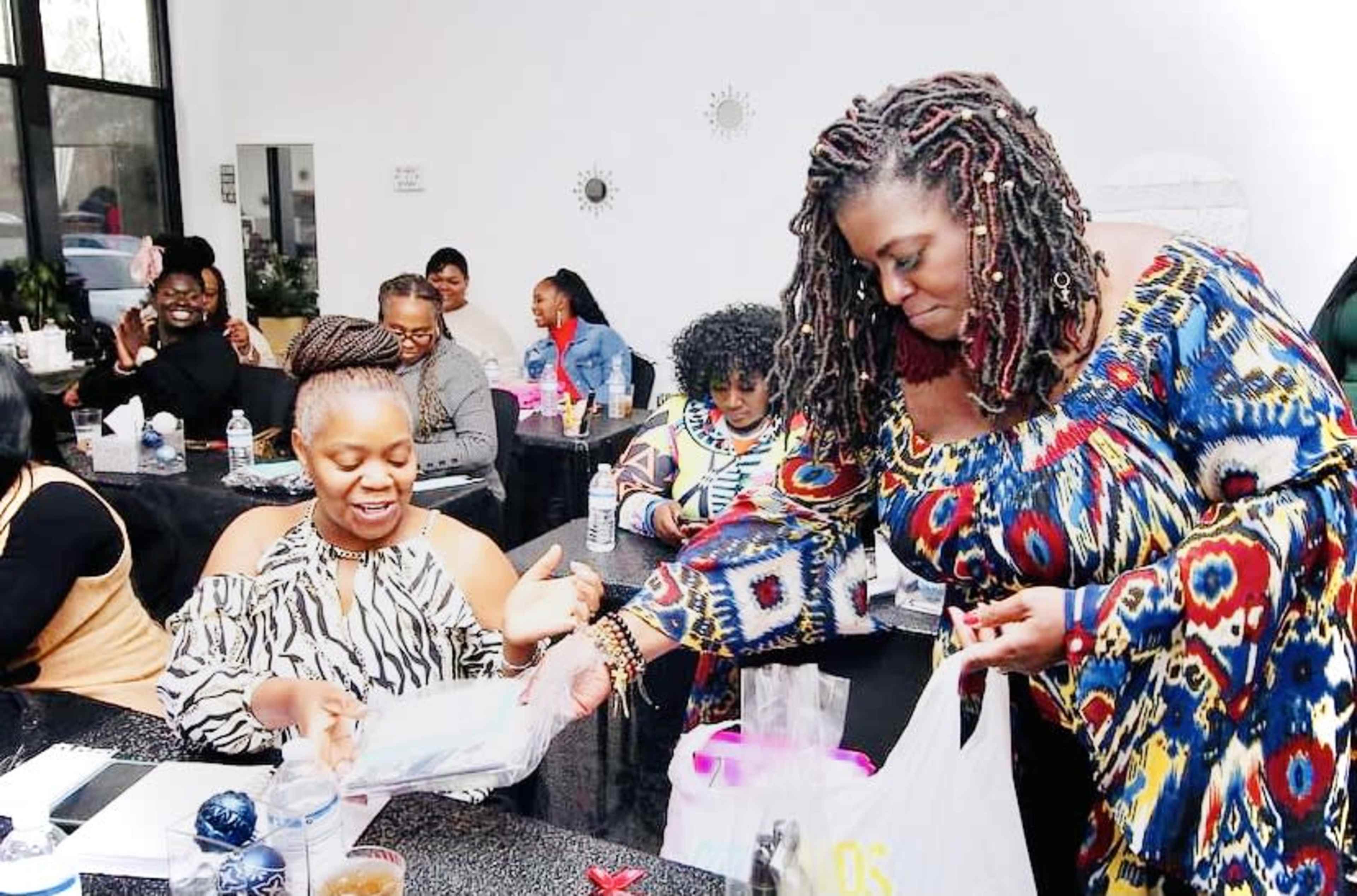 A group of women gathers around a table in a brightly lit room, engaging in conversation and exchanging items.