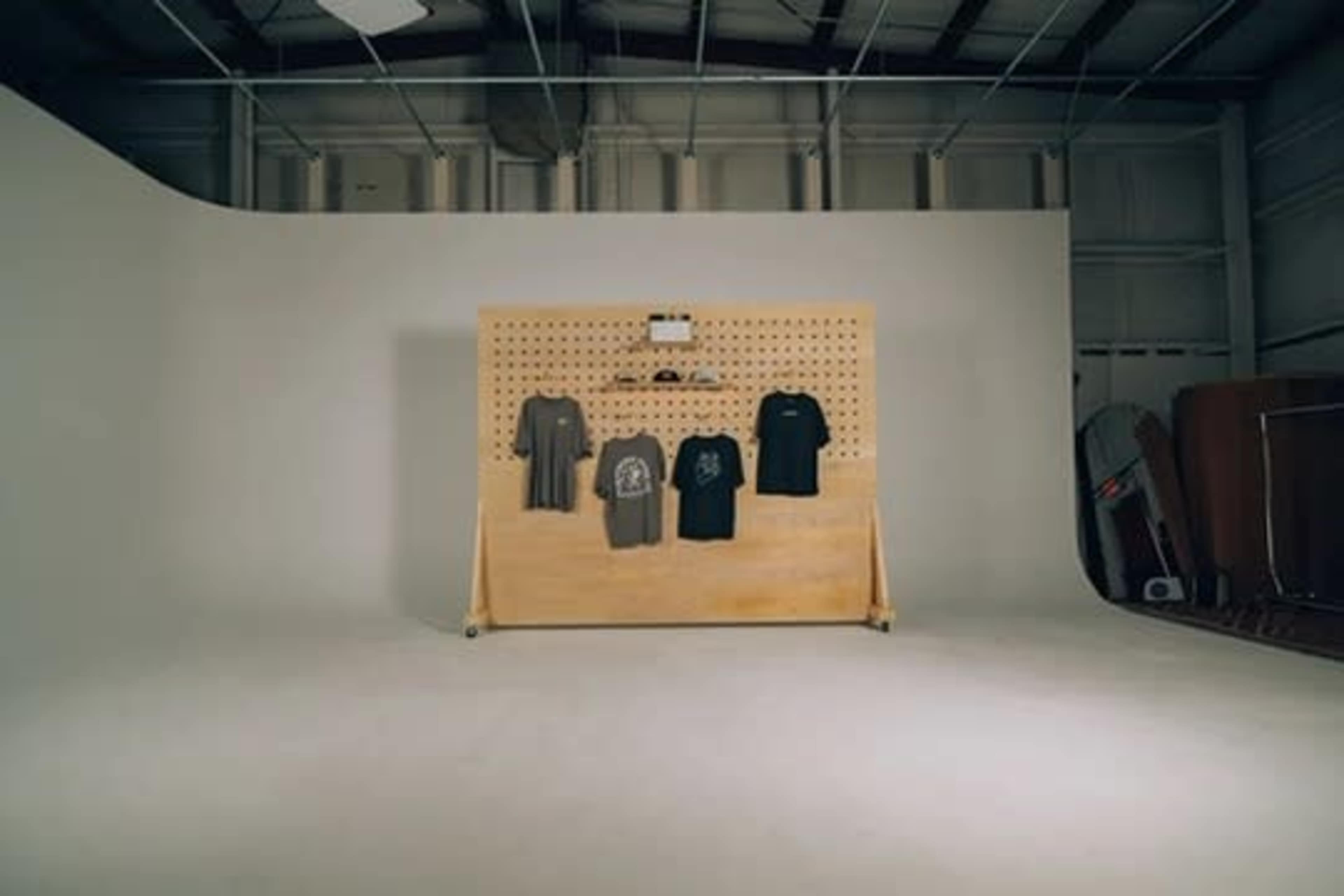 A simple display features five t-shirts hanging on a wooden pegboard in a spacious, well-lit studio.