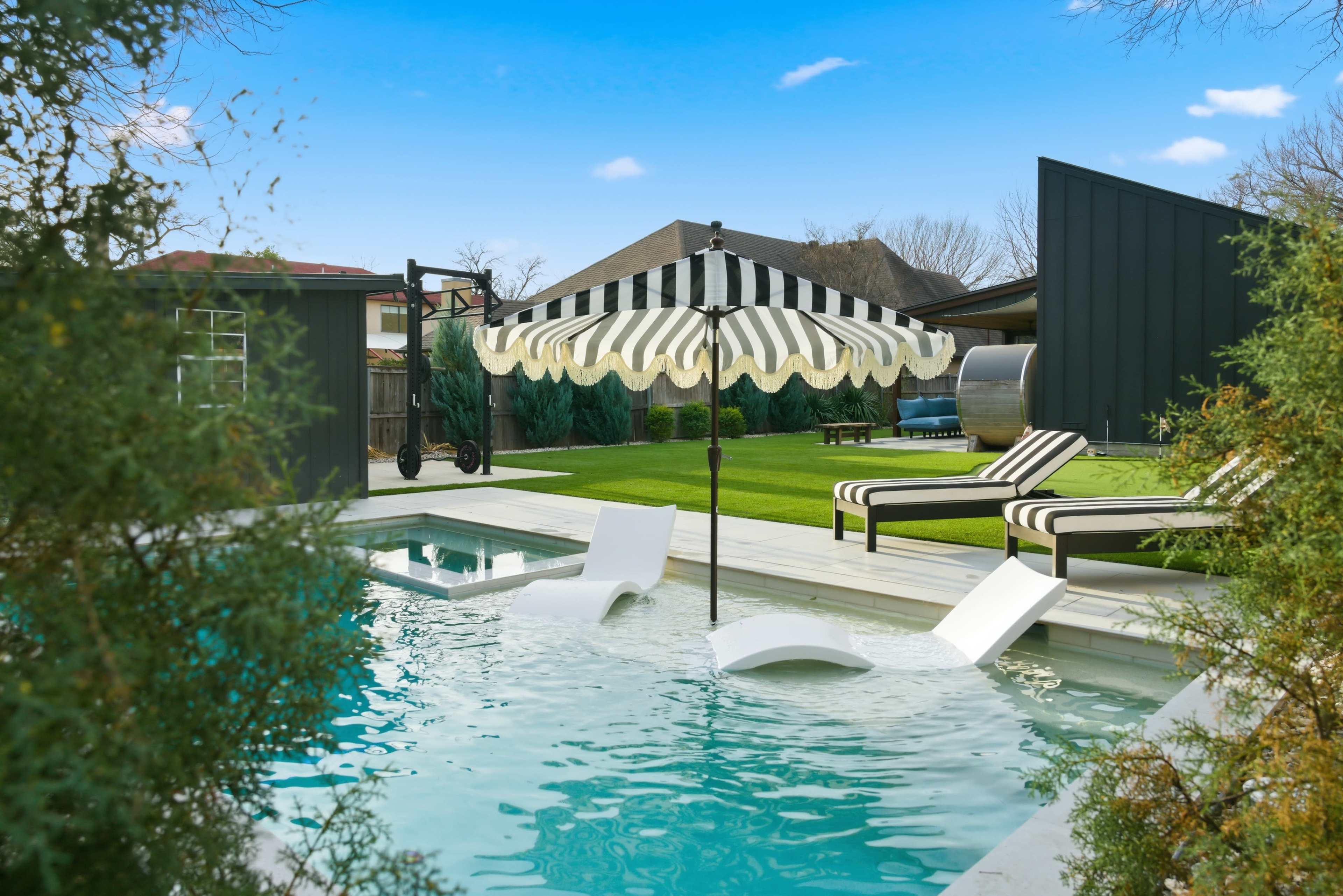 The image features a modern backyard pool area with a striped umbrella, lounge chairs, and a green grassy space behind it.
