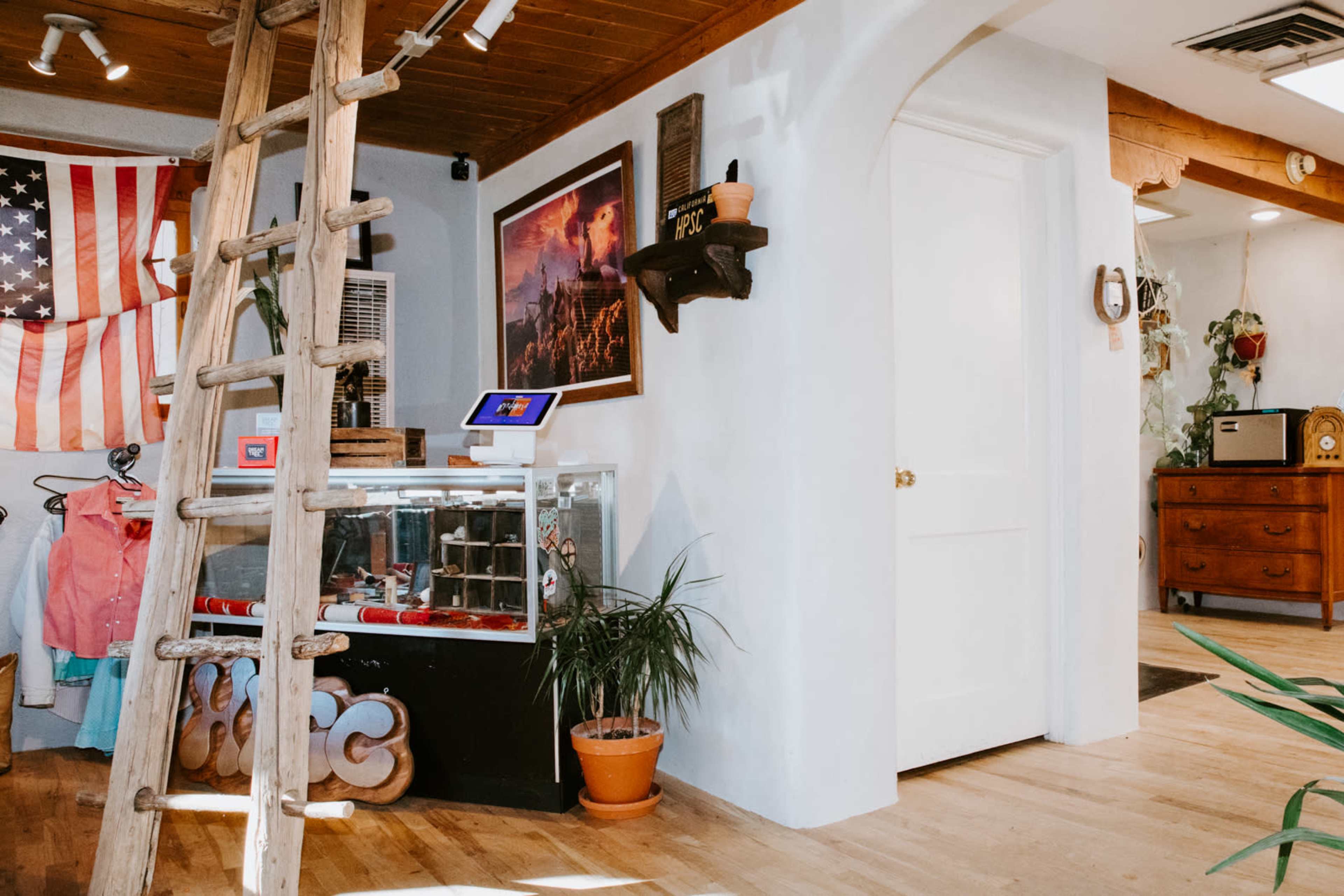The image shows an interior space featuring a wooden ladder, an American flag hanging on the wall, a display case with items inside, and a white door leading to another room.