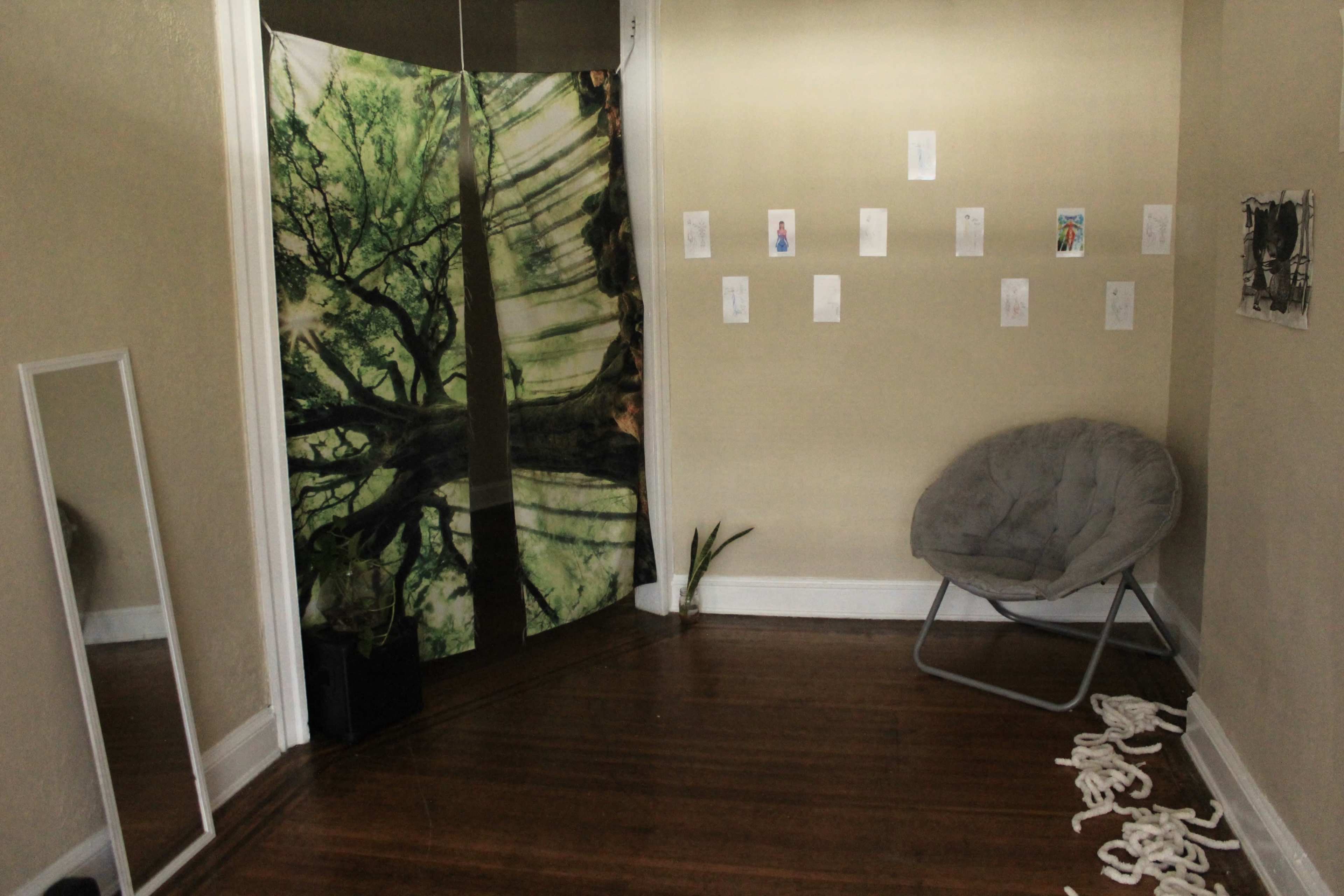 The room features a folding screen with a tree design, a gray chair, a plant, and several artworks displayed on the walls.