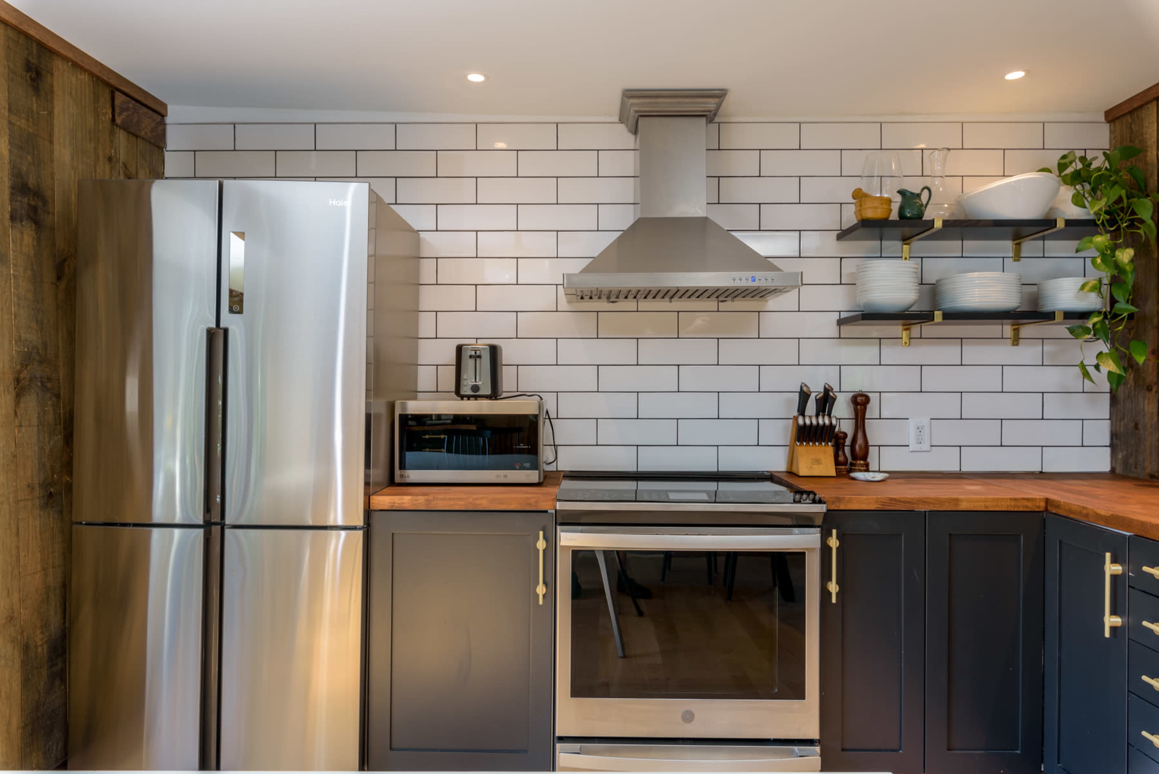 A modern kitchen featuring stainless steel appliances, a tiled backsplash, and dark cabinetry with wooden countertops.