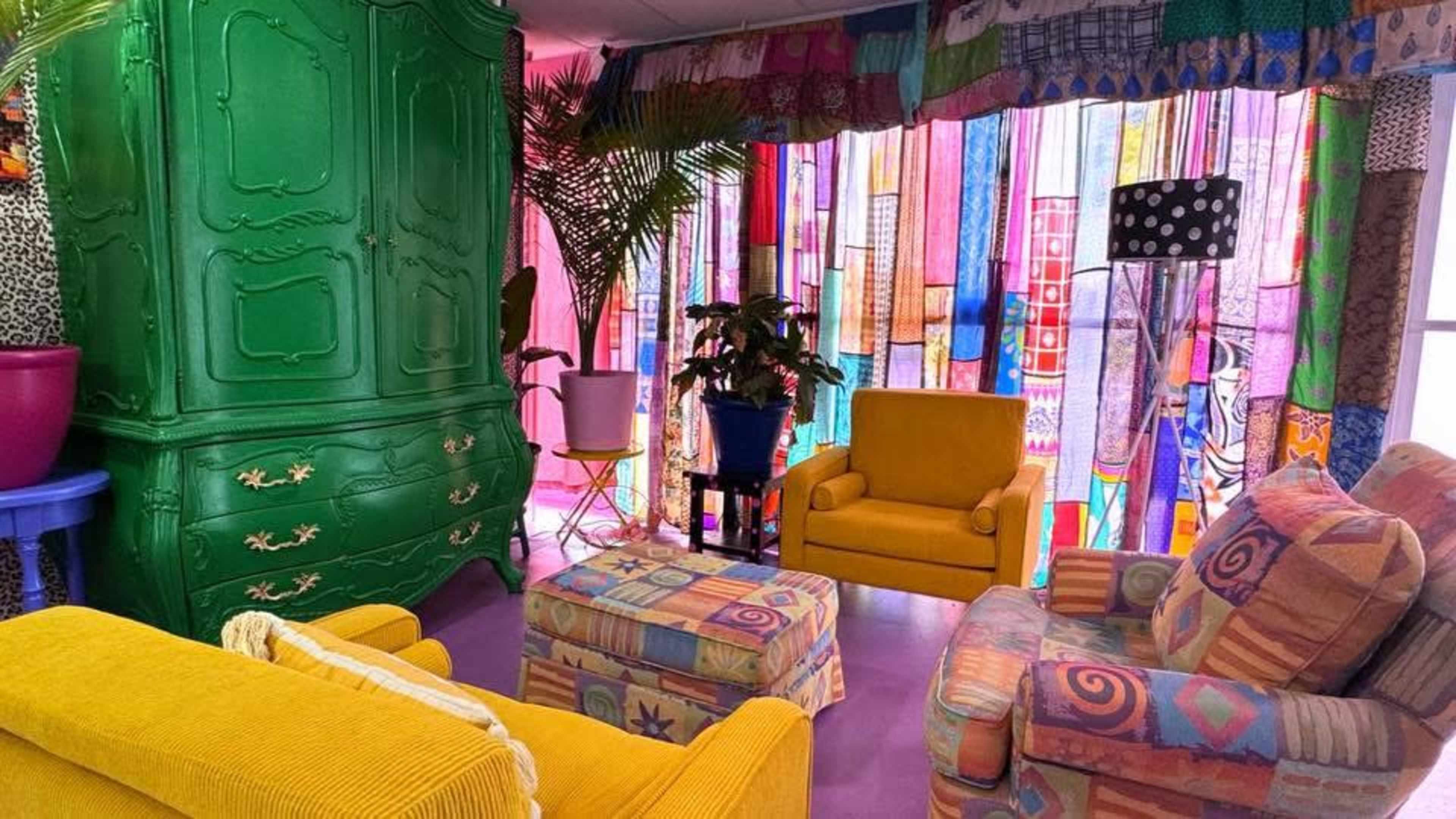 The room features brightly colored furniture, including yellow sofas and a green wardrobe, with vibrant fabric drapes creating a lively atmosphere.
