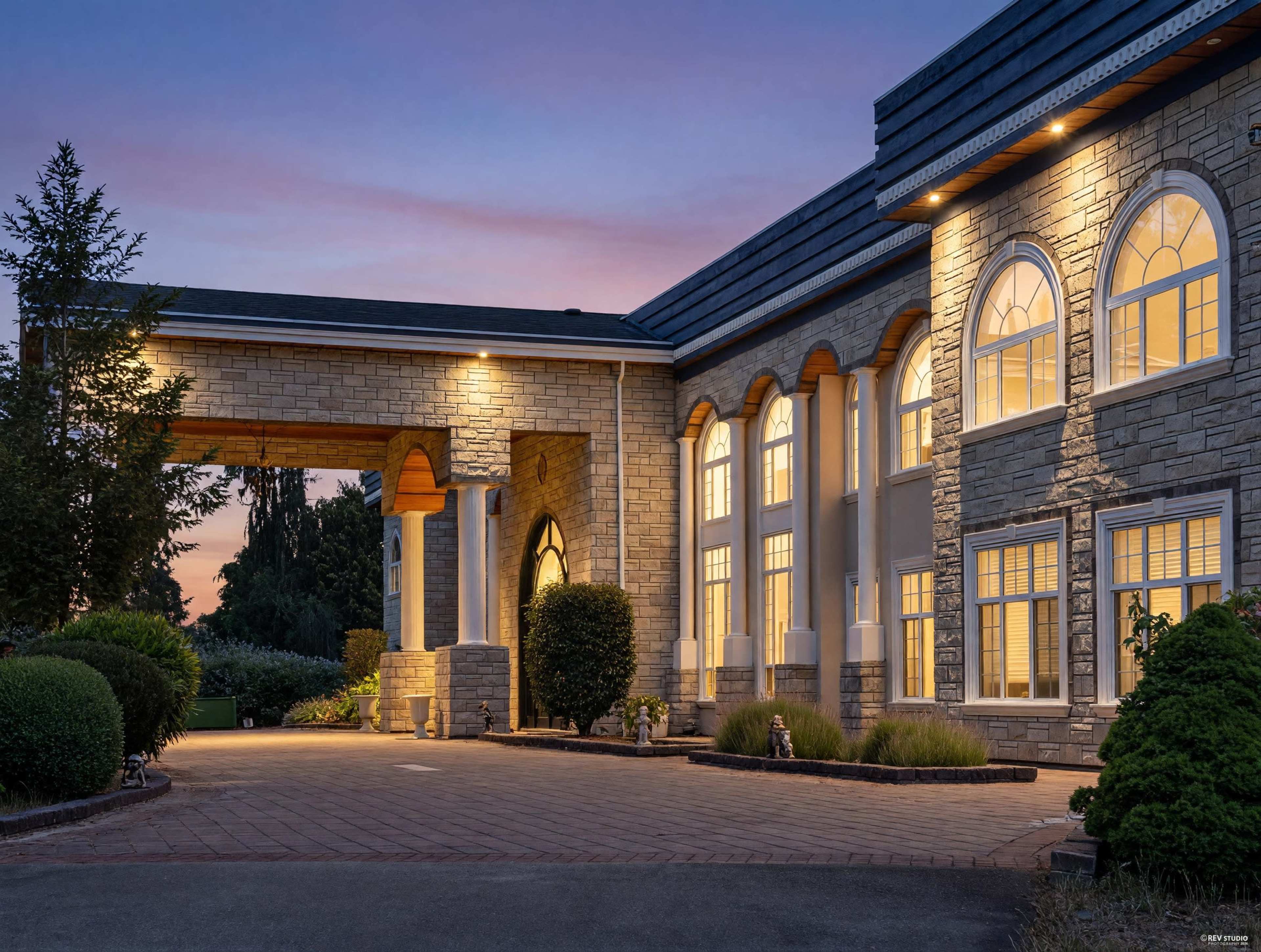 The image shows a large, elegantly designed home with stone accents and illuminated entry features at dusk.