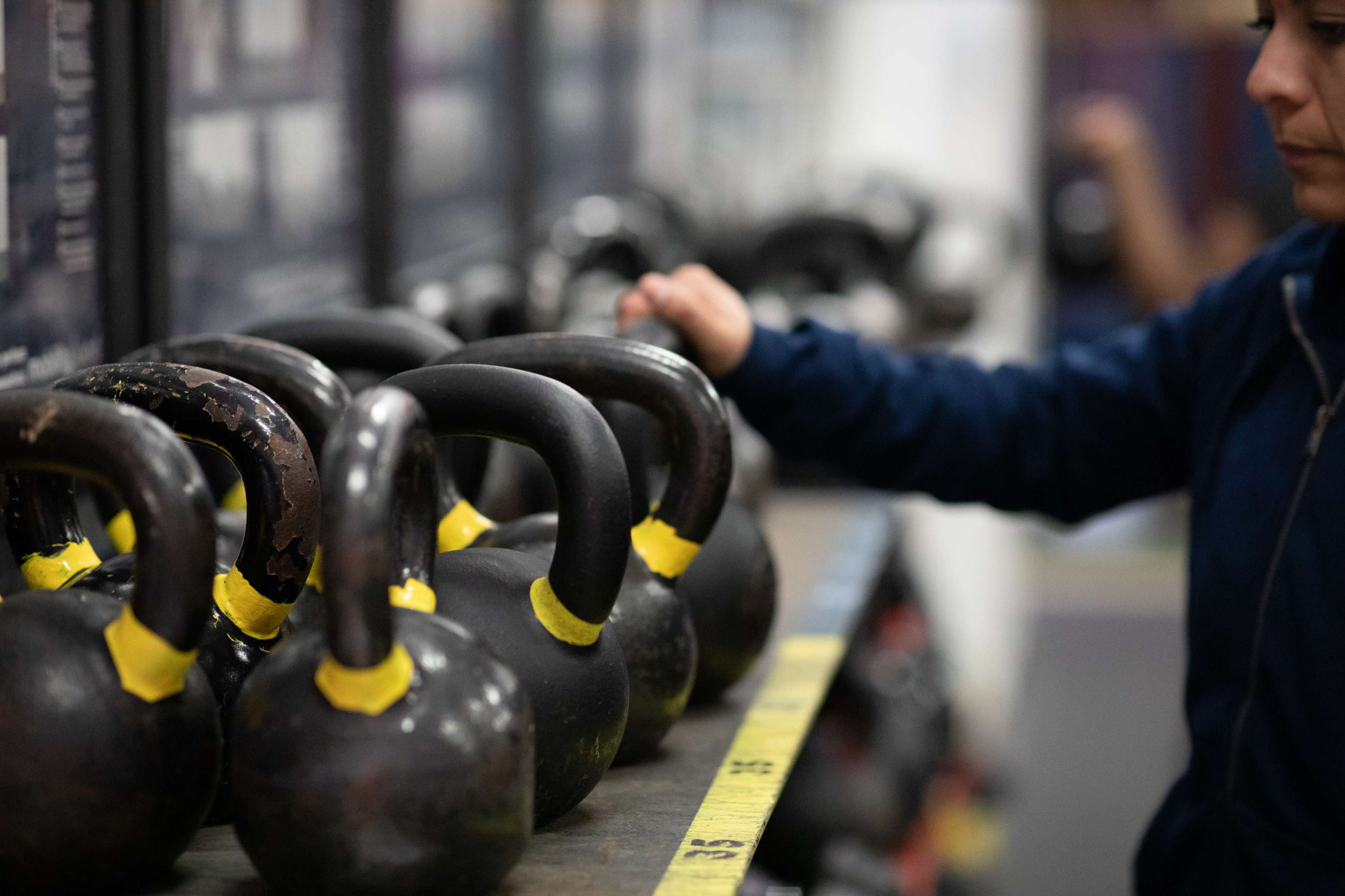 A person selects a kettlebell from a rack in a gym.