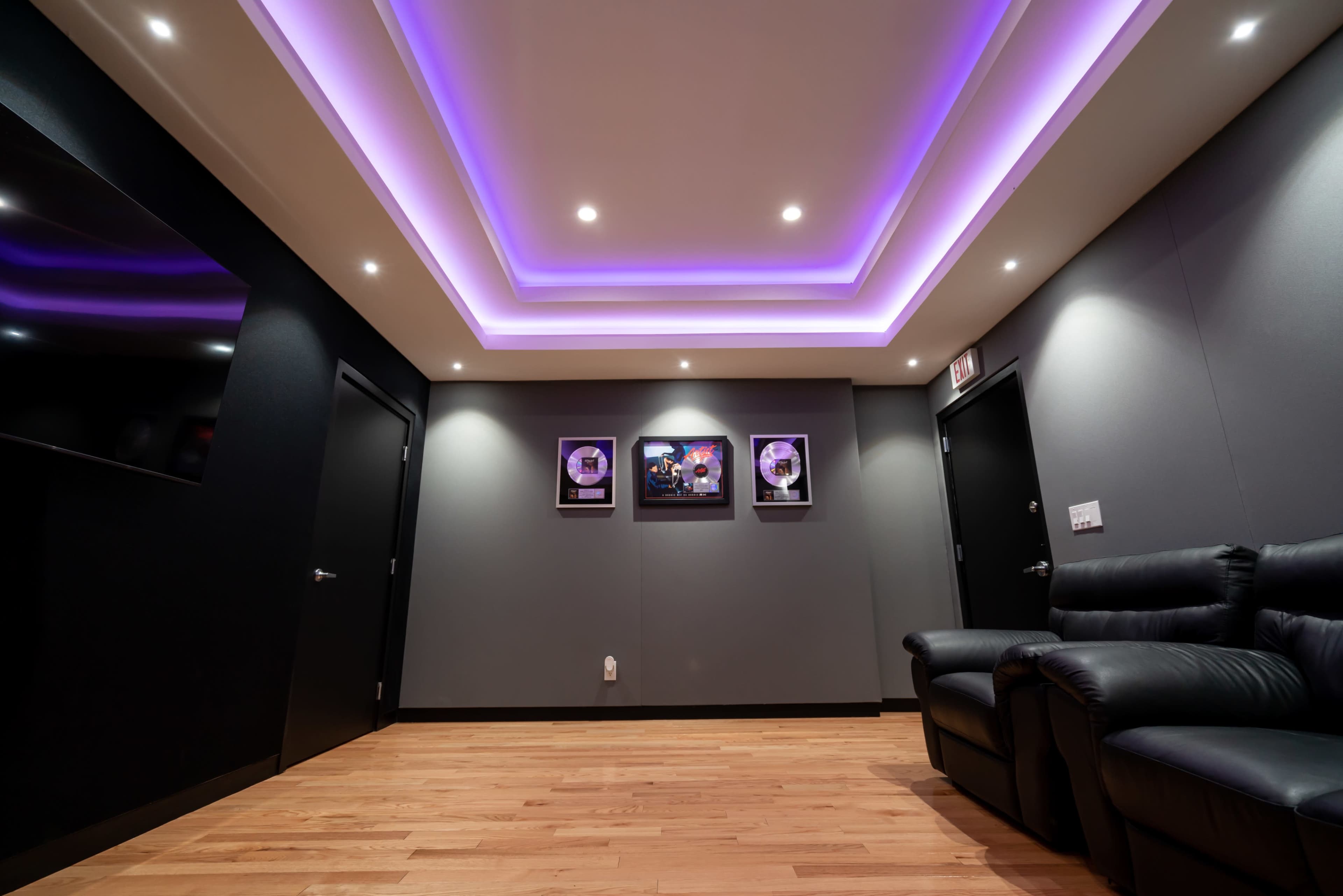 A modern interior space features a wooden floor, black walls, and a ceiling with purple lighting, displaying framed records on the wall.