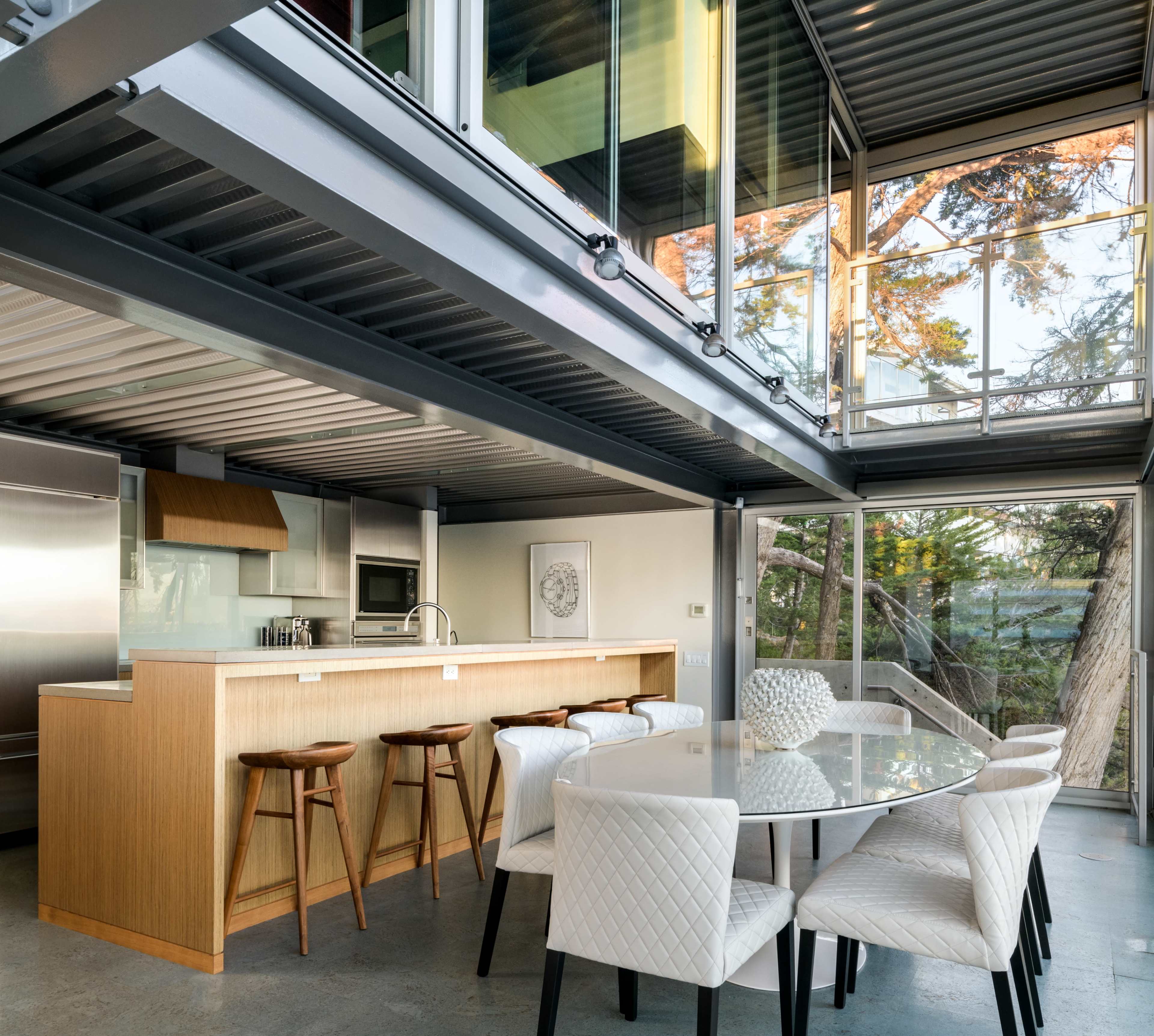 A modern kitchen and dining area with large windows, a wooden island bar, and sleek dining furniture.