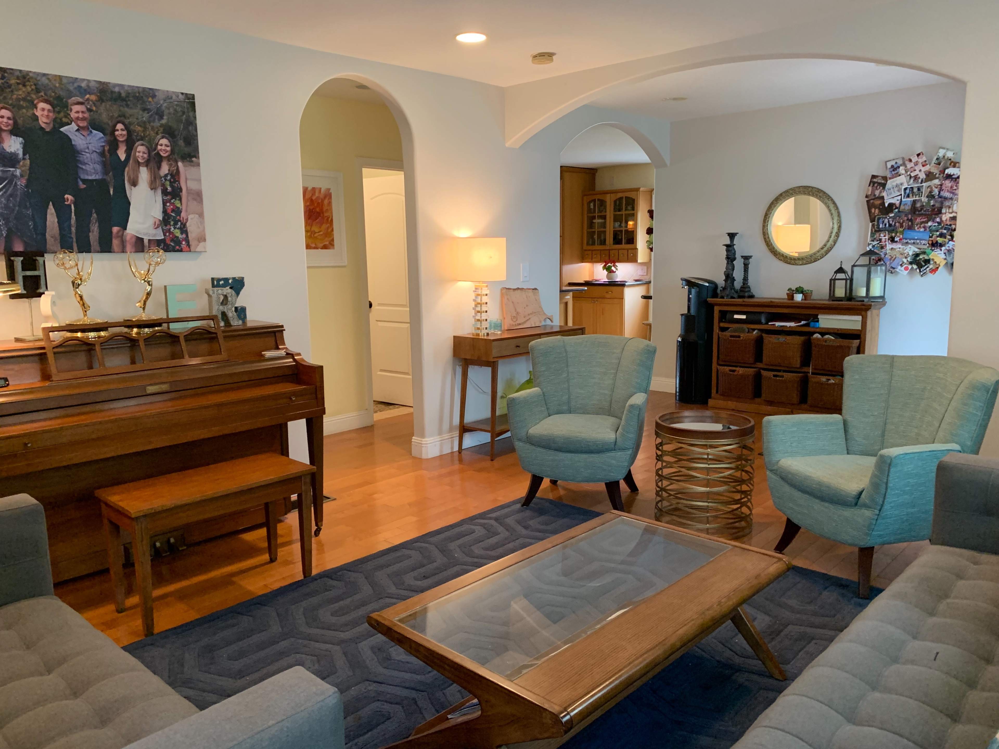 A cozy living room with a piano, two armchairs, a sofa, a coffee table, and a gallery wall featuring family photos.