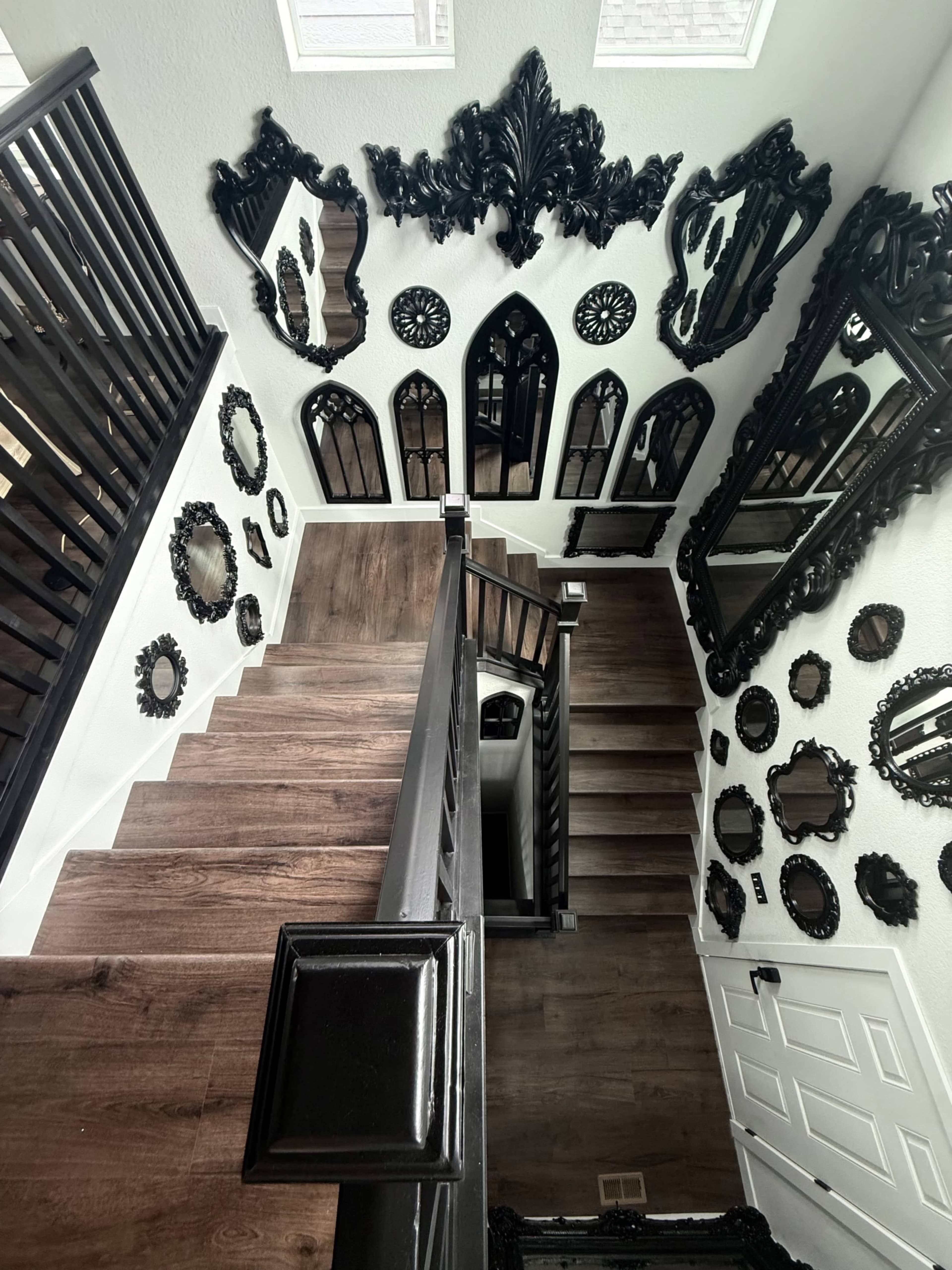 The image depicts a staircase with dark wood steps surrounded by an array of black ornate mirrors on the walls.