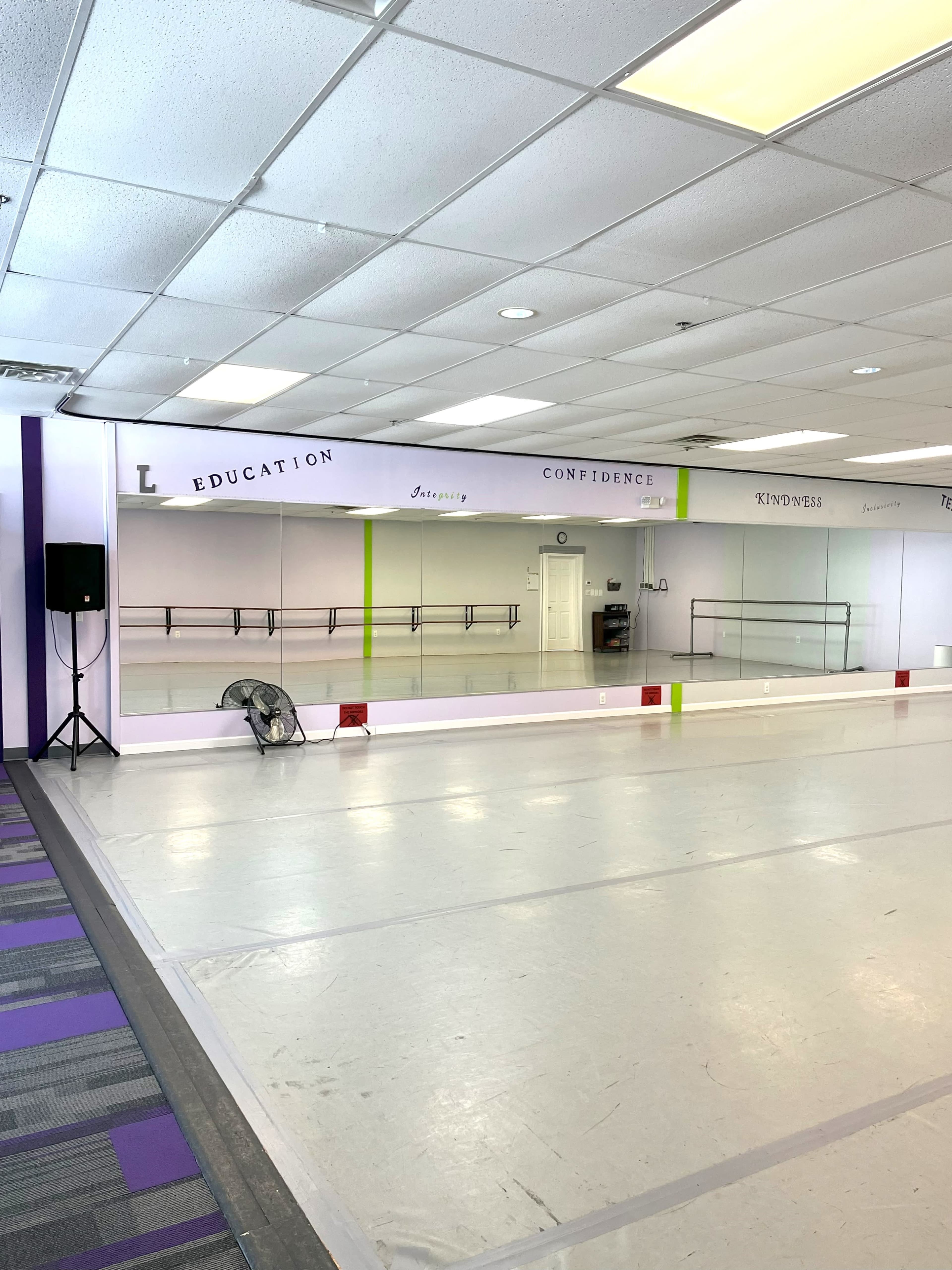 The image shows a dance studio with mirrored walls, a fan in the corner, and motivational words displayed along the top of the walls.